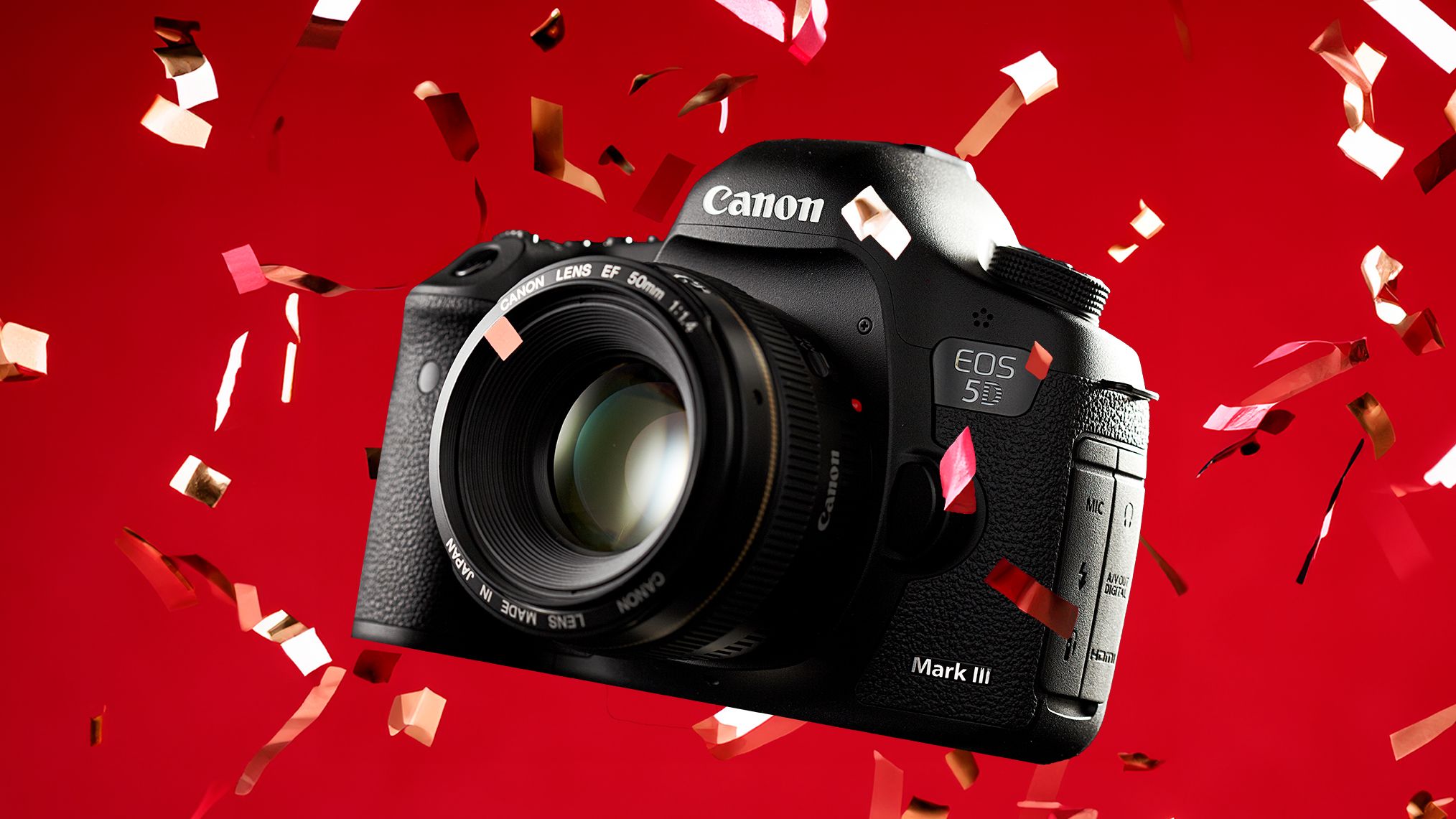 A Canon EOS 5D Mark III camera surrounded by colorful confetti against a vibrant red background, showcasing its sleek design