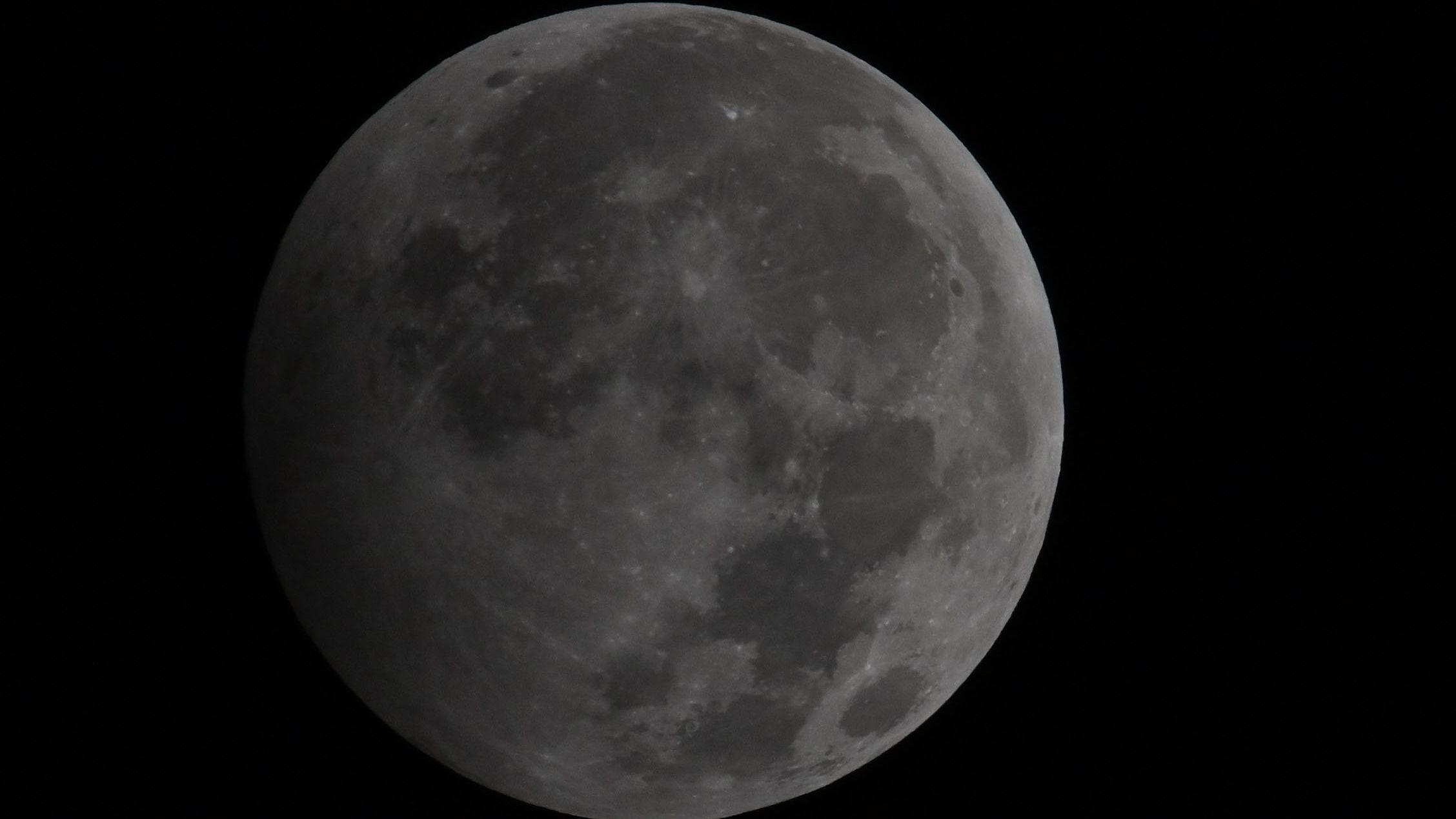 A photograph showing the penumbral stage of a lunar eclipse as the lunar disk shines in a black night's sky.