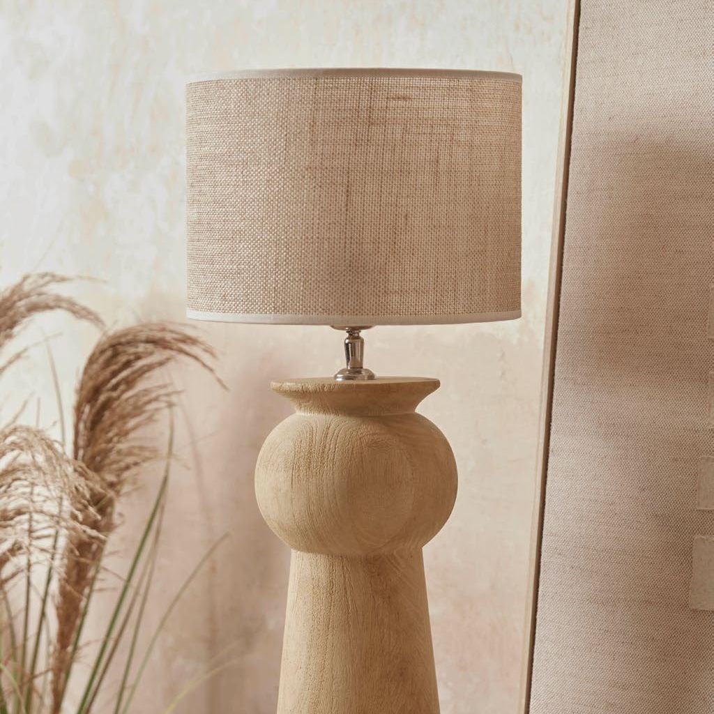 Carved mango wood table lamp with a drum shade next to a mirror and plaster coloured wall