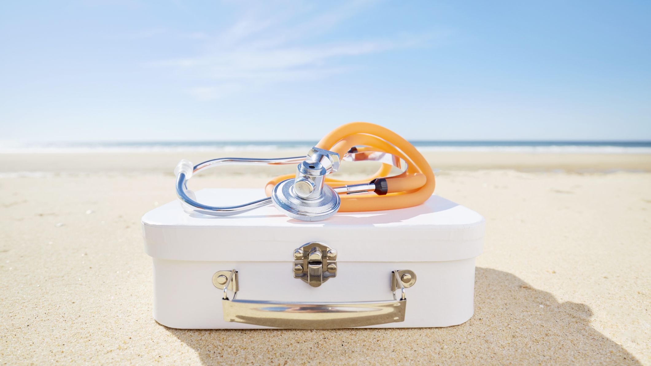 Stethoscope and suitcase on beach by the sea.