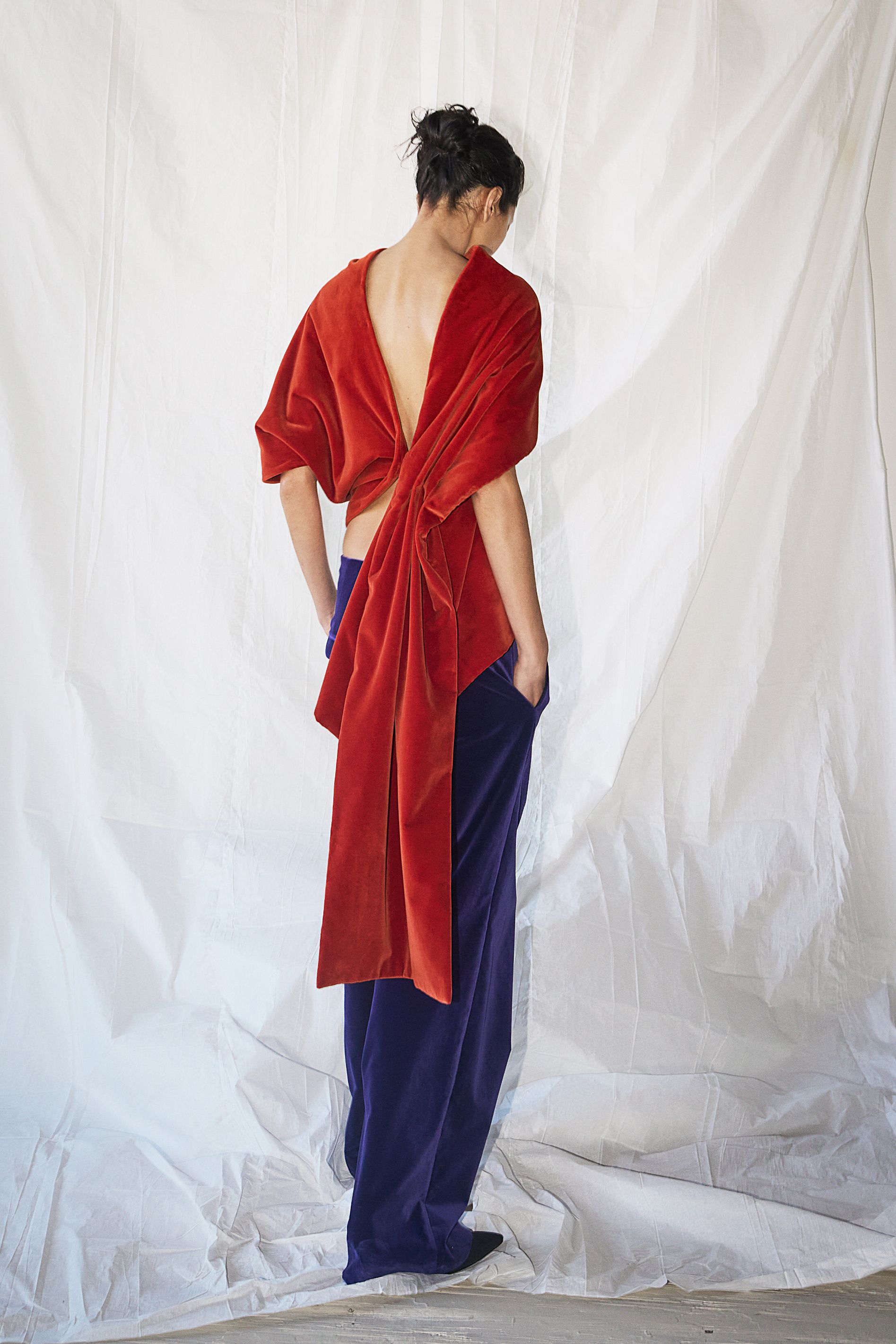 A model wearing a persimmon orange colored velvet draped blouse and dark purple velvet pants in Colleen Allen's Fall 2026 collection