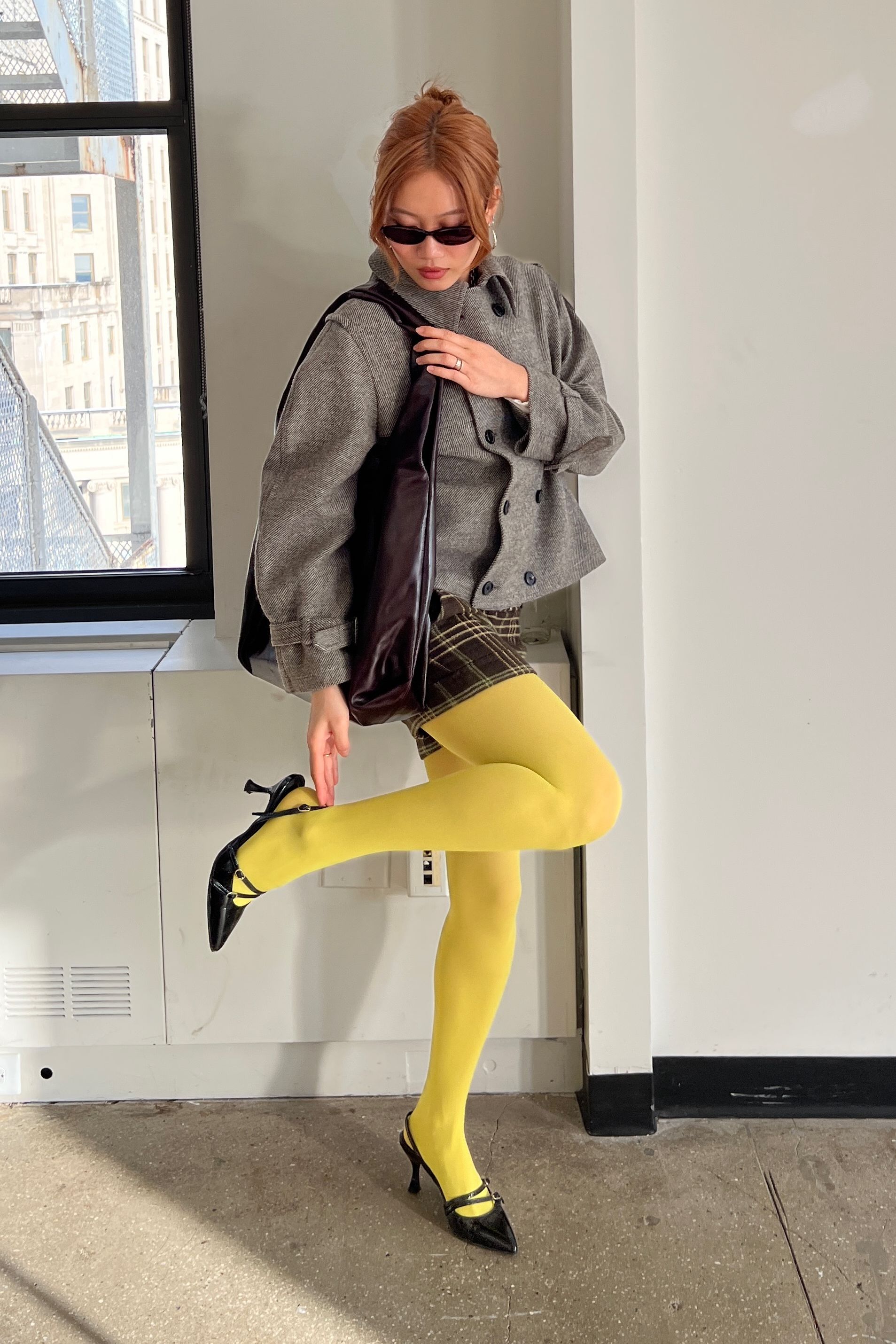 Vivian Li wearing a grey jacket, brown plaid skirt, and yellow colorful tights at Paris Fashion Week.