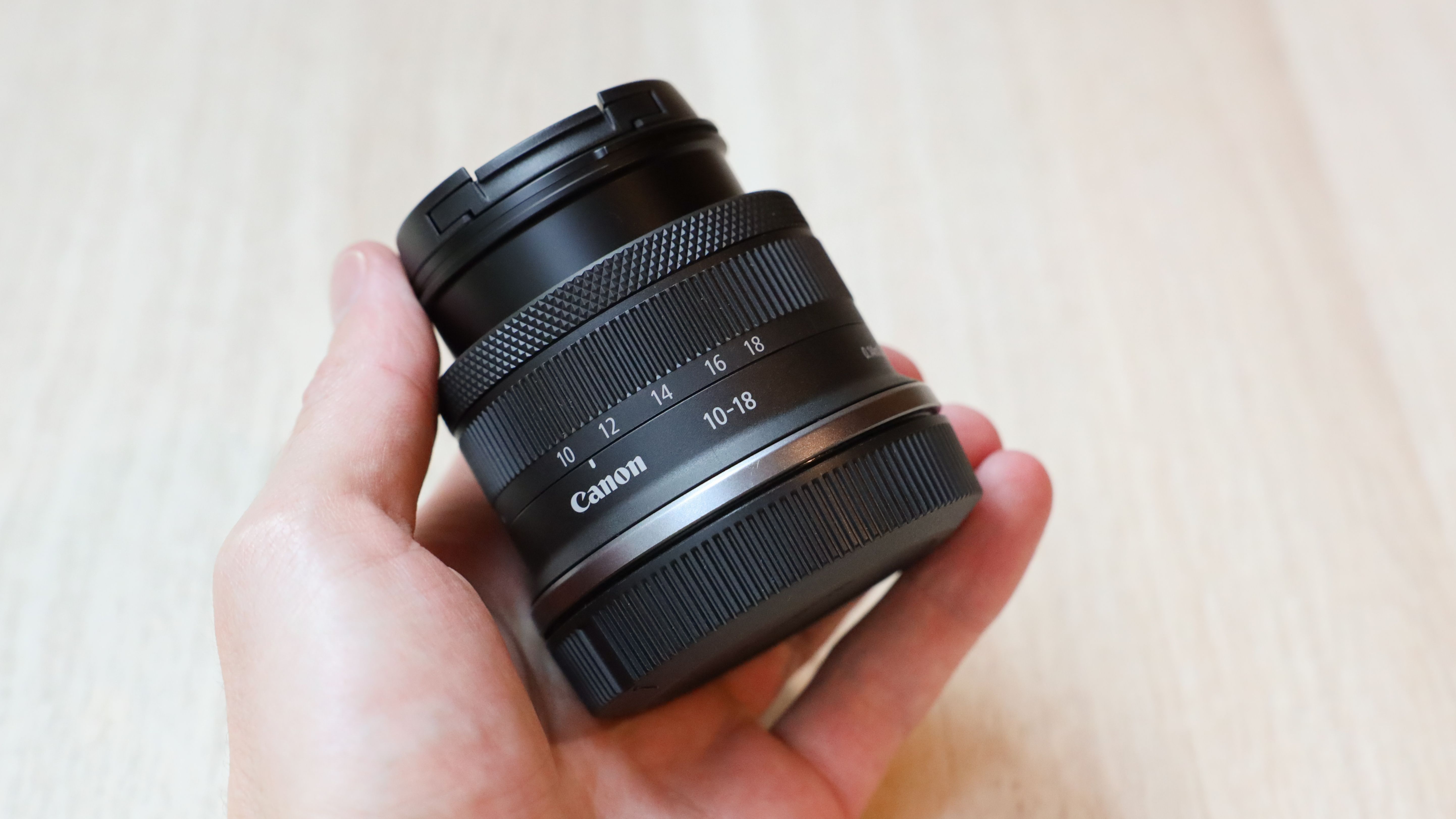 A Canon RF-S 10-18mm f/4.5-6.3 IS STM lens held in a hand