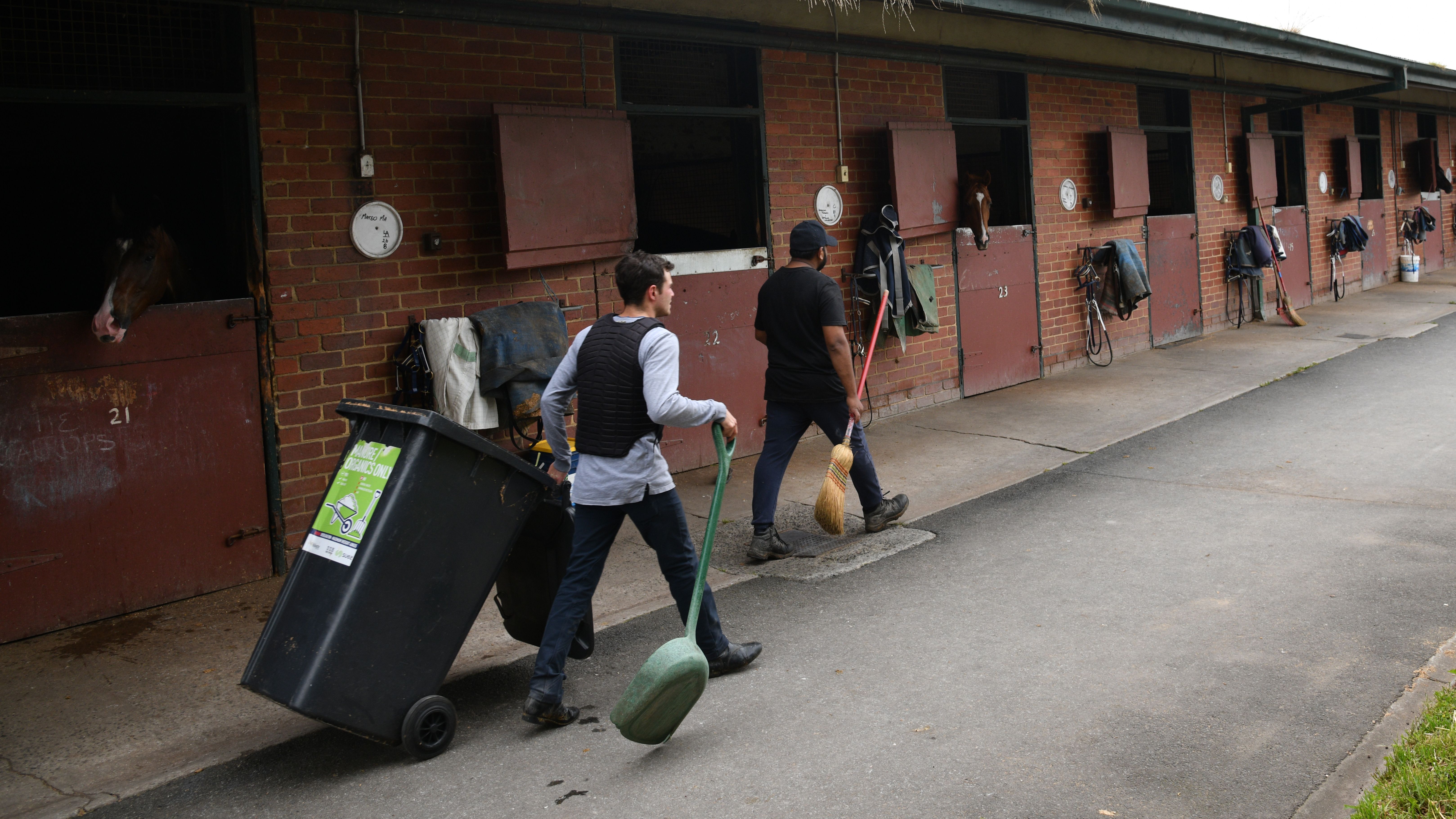 Man wheeling a bin outside a stable block