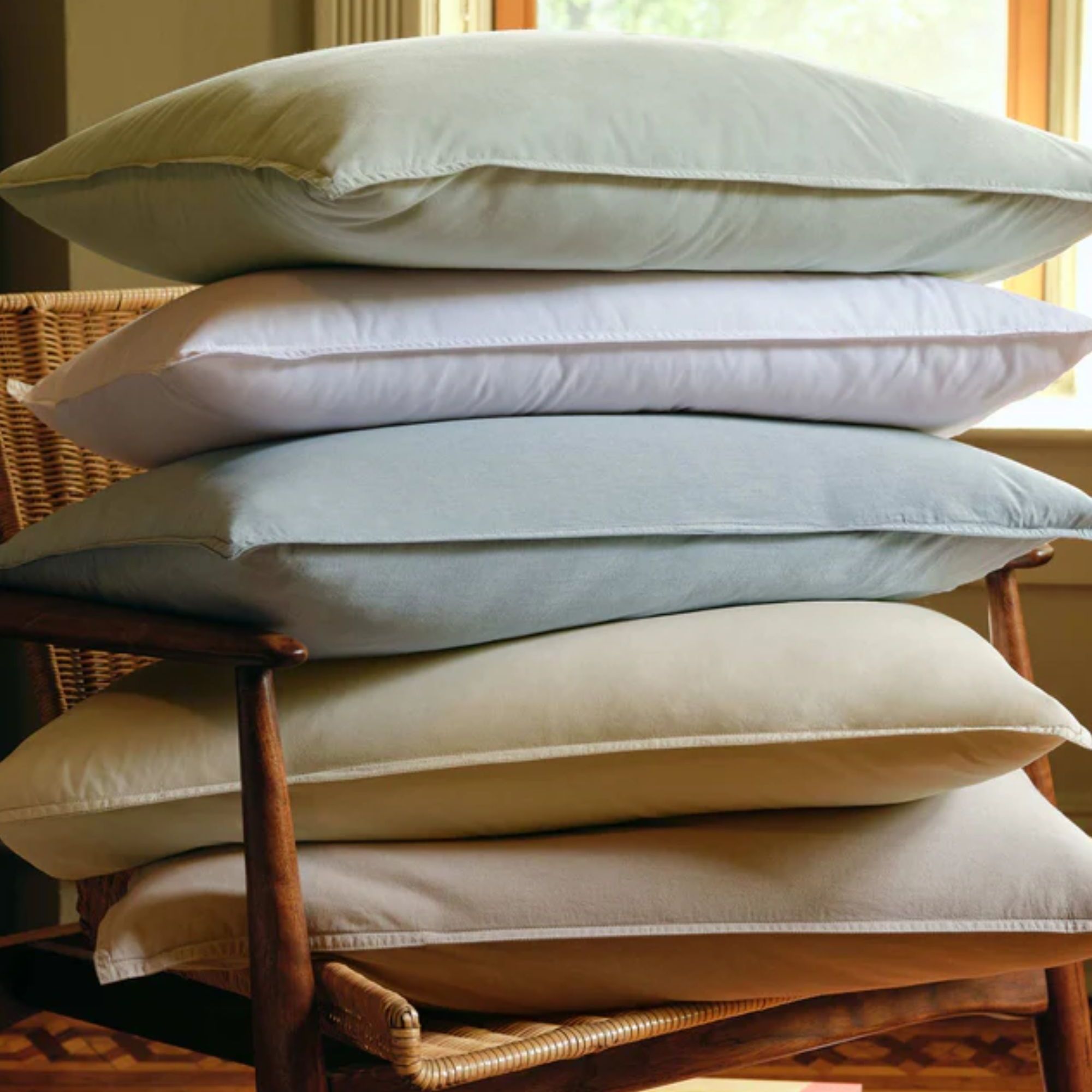 Stack of pale green, blue, yellow and cream pillows on a wicker chair