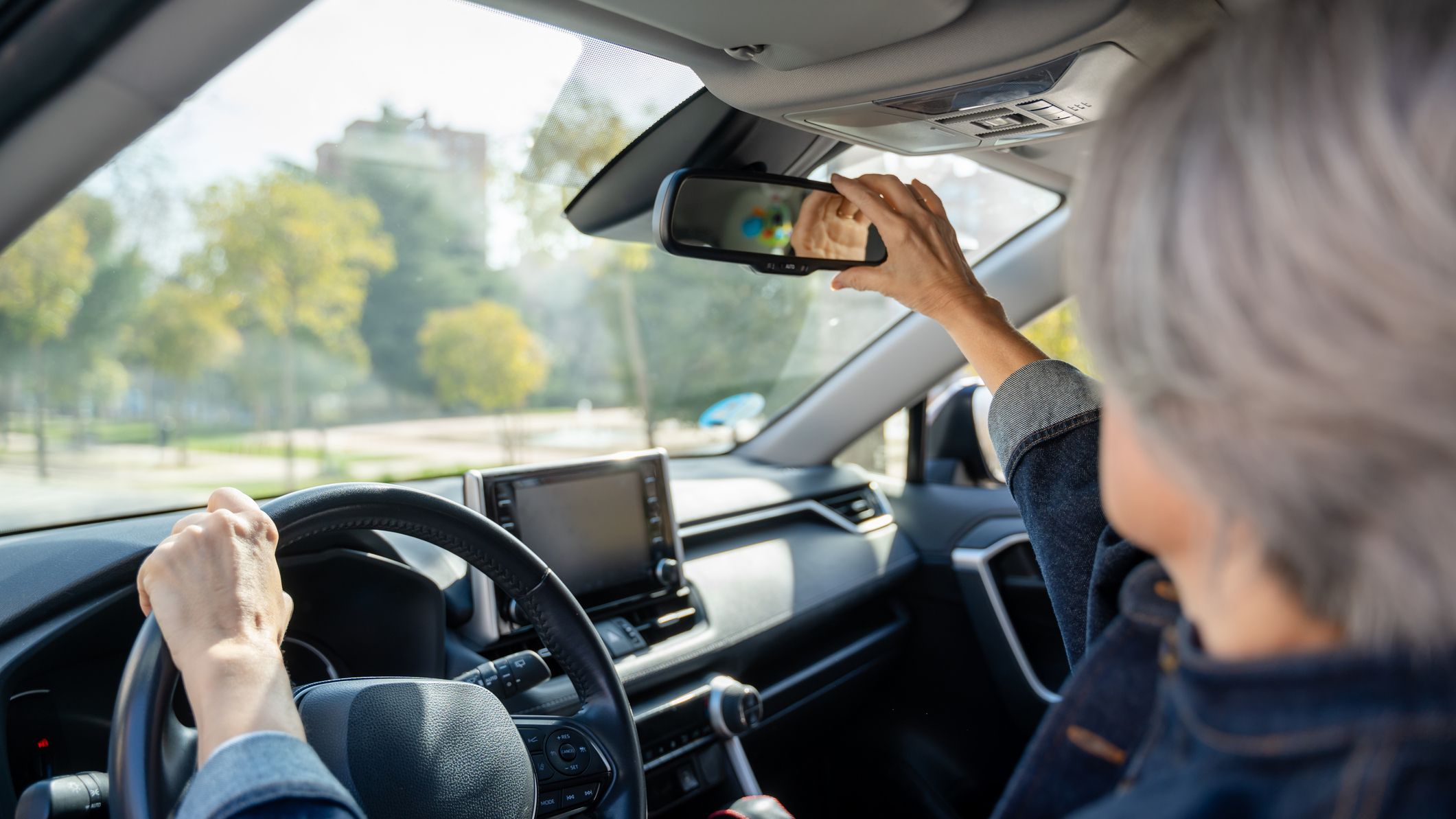 Woman adjusting rearview mirror while driving car