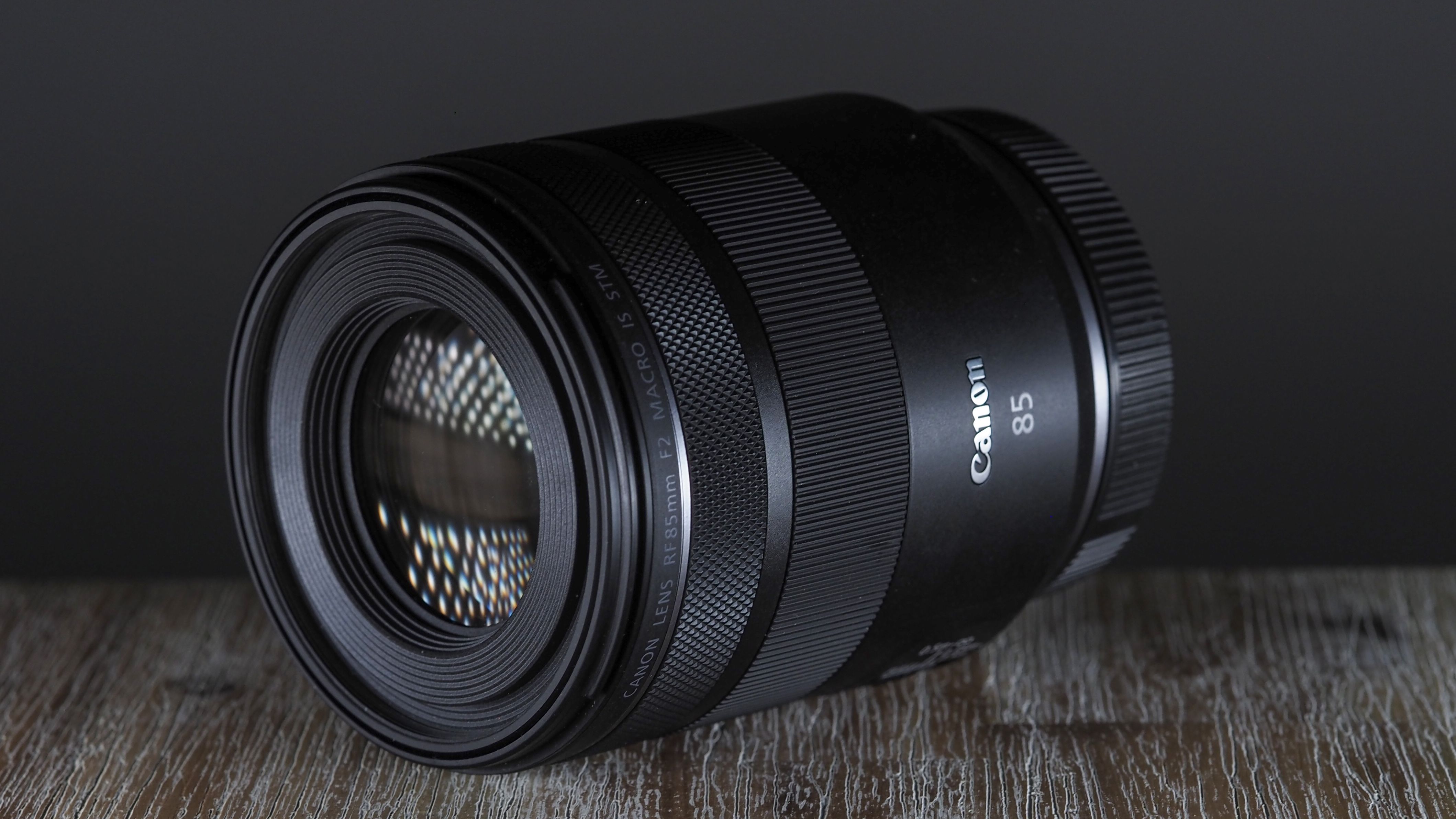 Canon RF 85mm f/2 Macro lens on a table, against a dark backdrop
