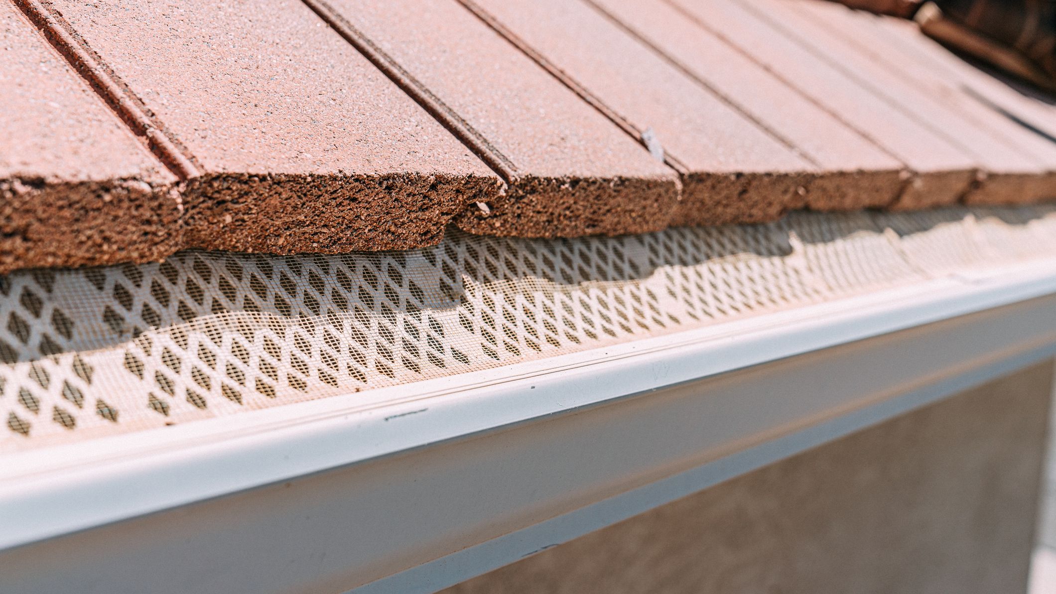 Mesh guard protecting an aluminum rain gutter from debris on a clay tile roof.