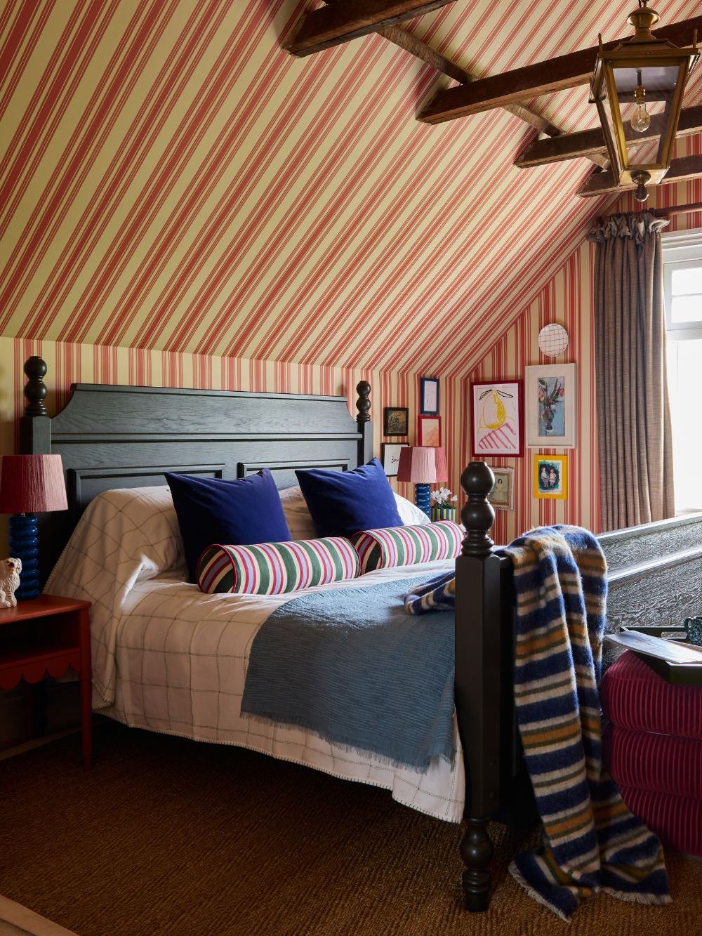a traditional english bedroom with a vaulted high beamed ceiling, stripe drenched walls and ceiling, a dark wooden bed, and striped pillows and throw