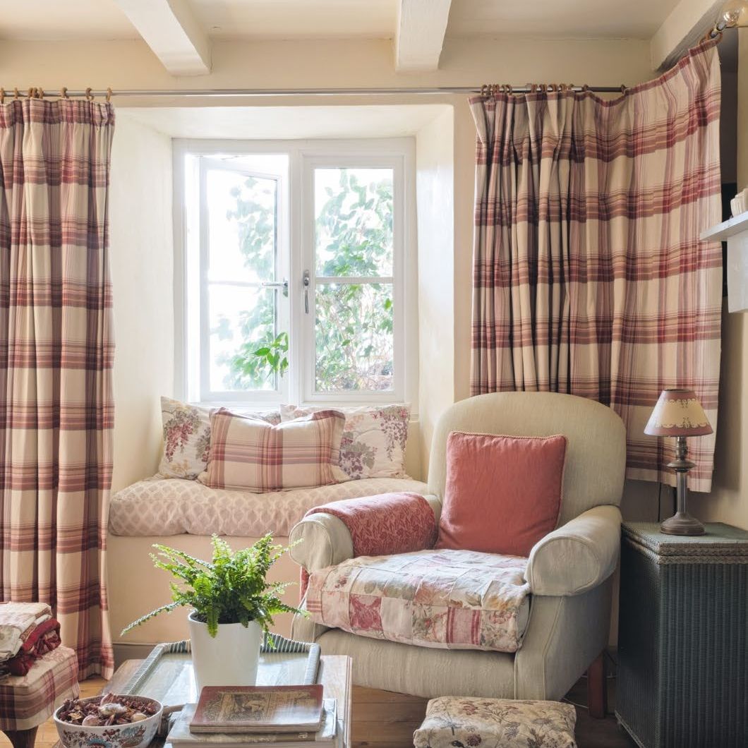 View towards window seat in a cosy cottage living room, with check curtains, old armchair and floral fabrics