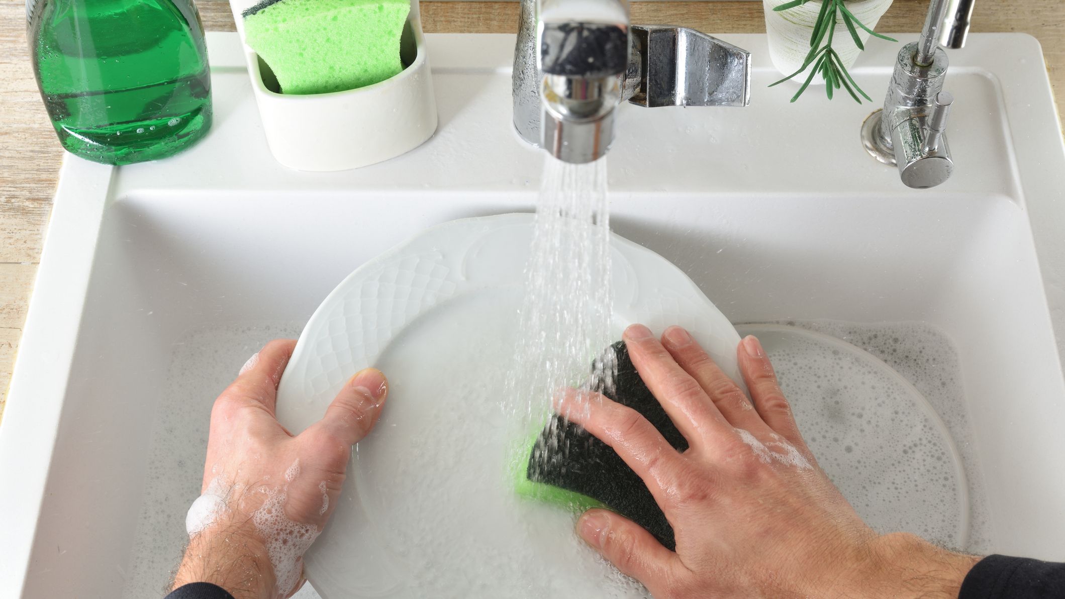 A person handwashing a dish under running water.