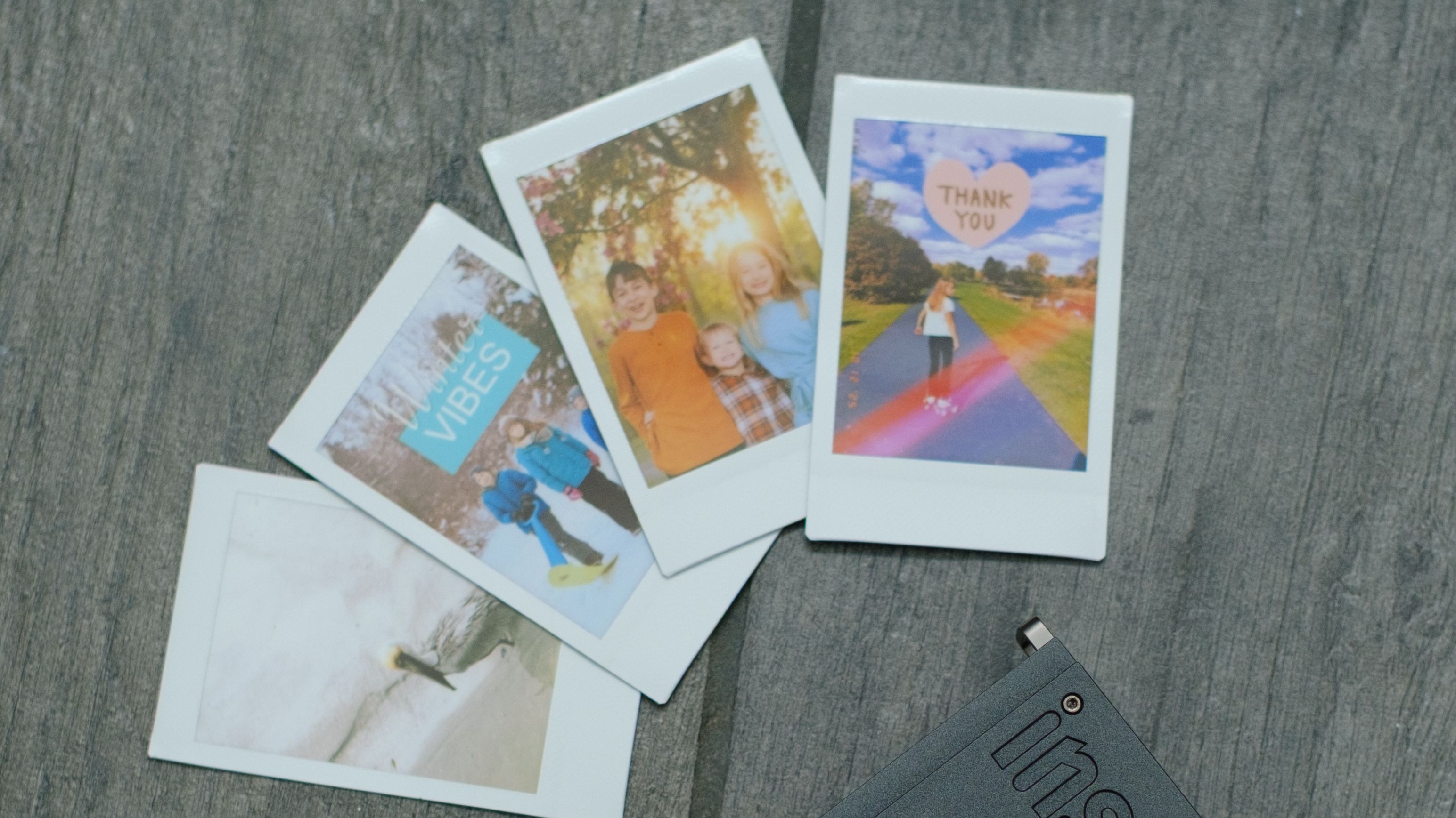 The Fujifilm Instax Mini Link+ on a gray background with instant prints