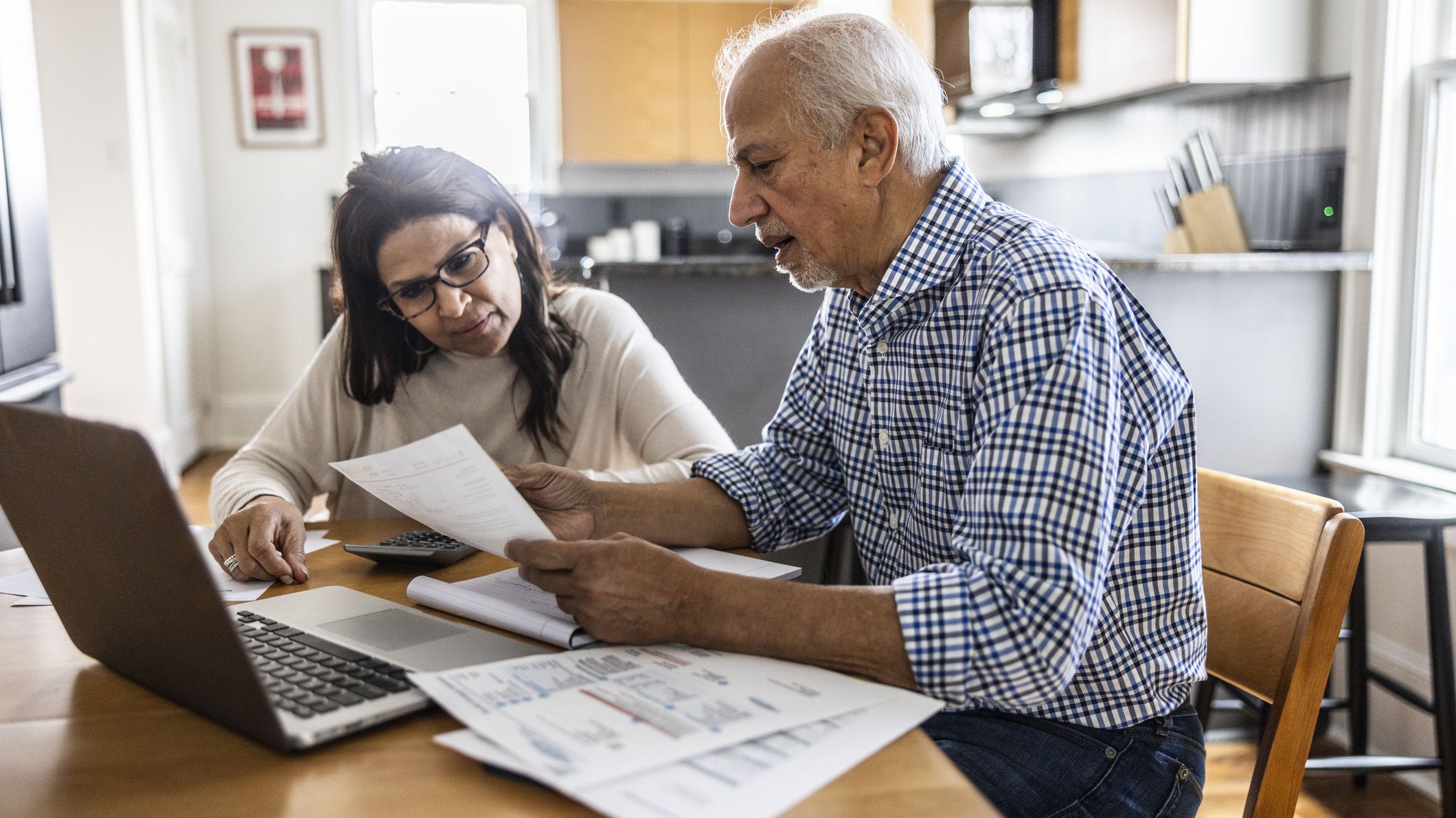 A senior couple discusses finances at dining table.