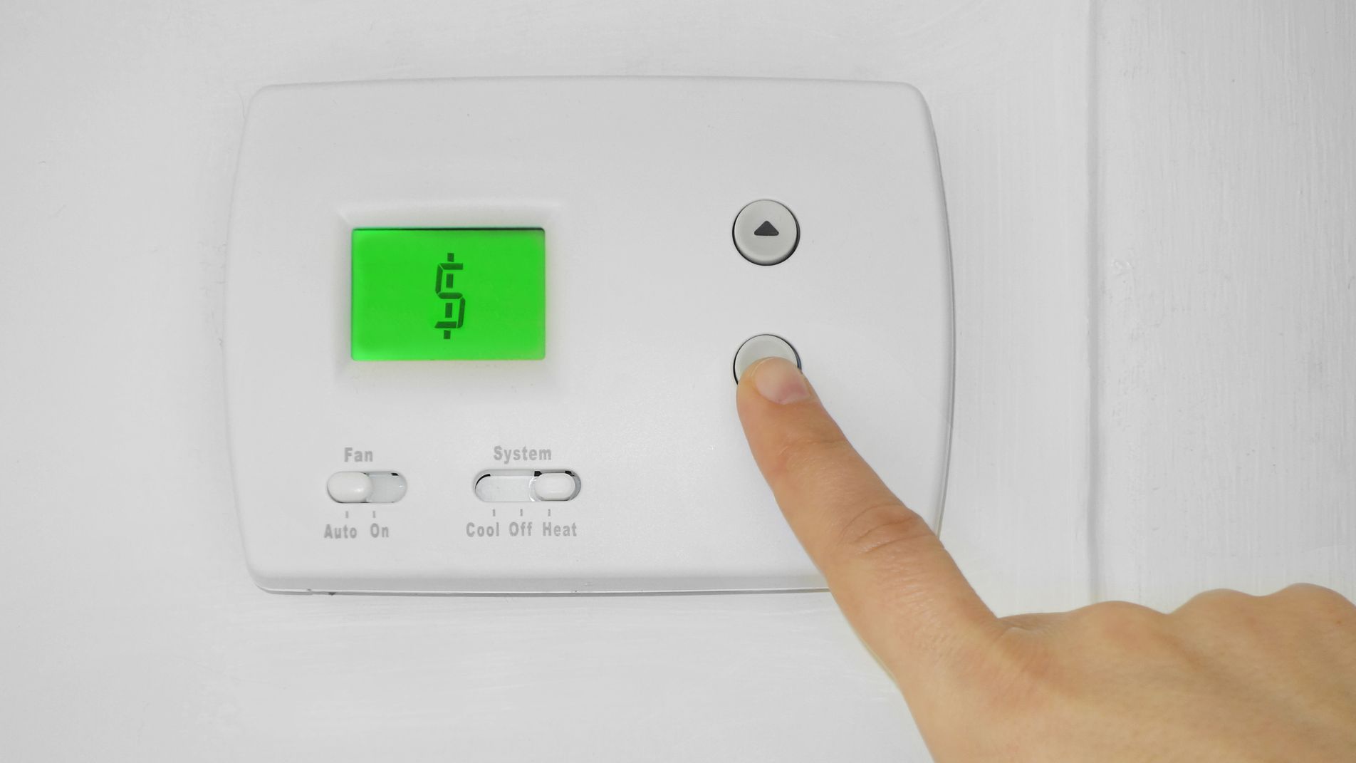 Finger pressing a button on a thermostat that displays a dollar sign, indicating rising energy costs.