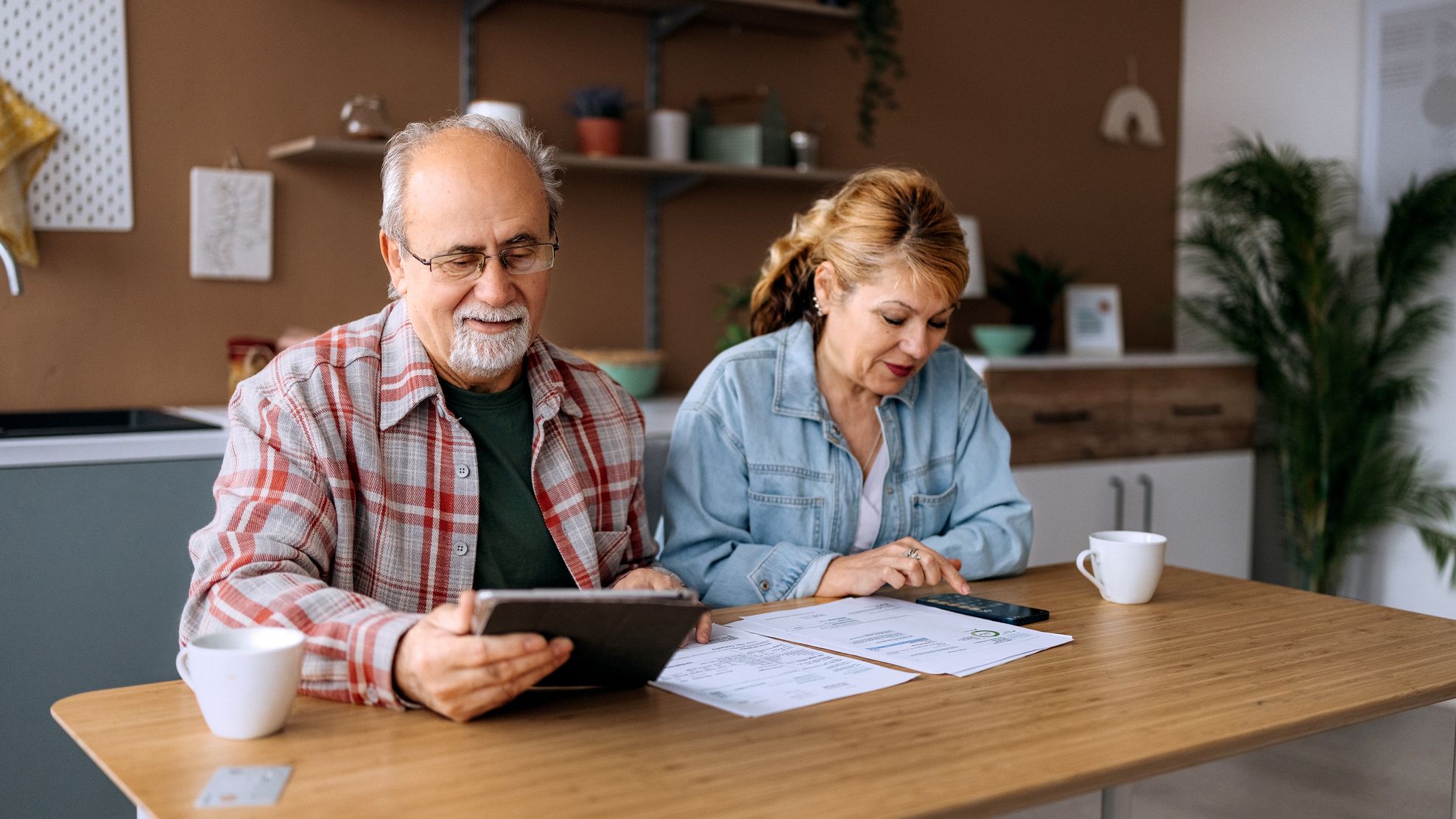 A mature couple sits together at home, reviewing expenses and bills.