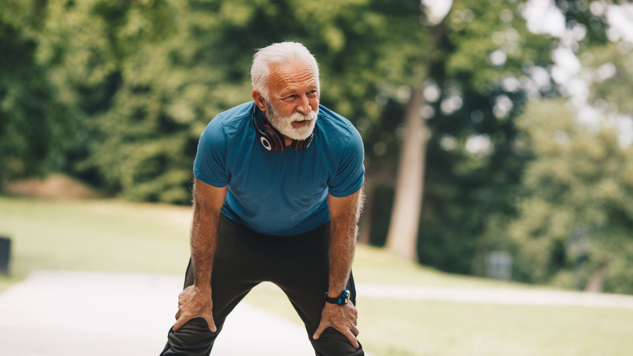Senior man is resting after warming up exercises. He is going to continue working out, stretching and jogging, but for now he will take deep breath.