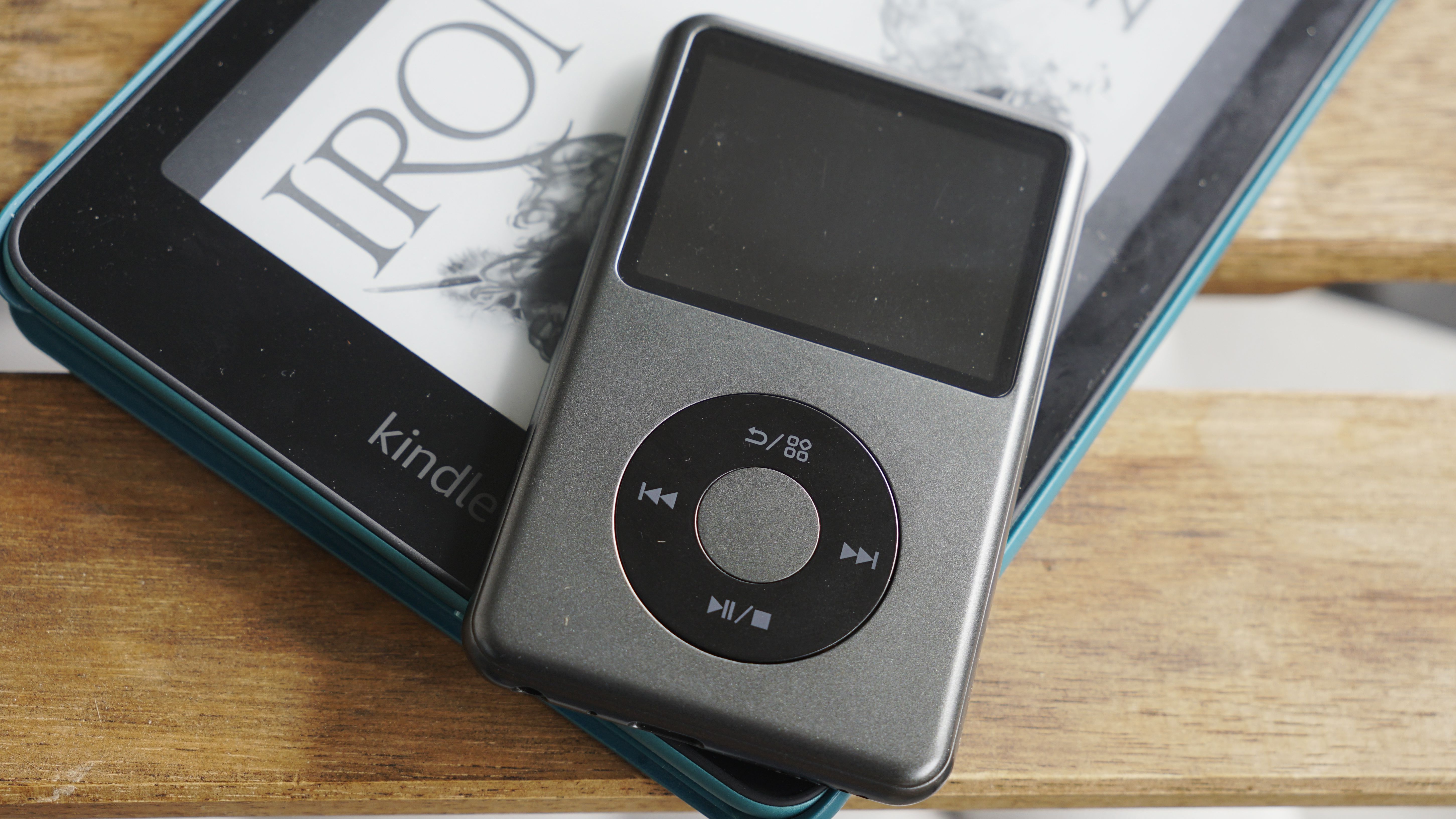 Innioasis Y1 player held in a man's hand, showing the dial and screen, with a wooden table in the background