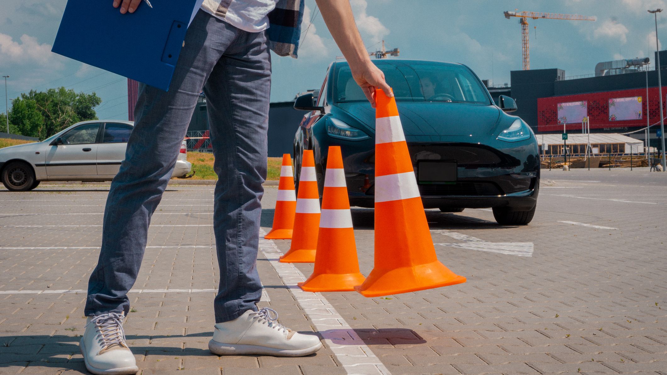 Male driving instructor standing with orange traffic cones and clipboard in his hands during exam outdoors.