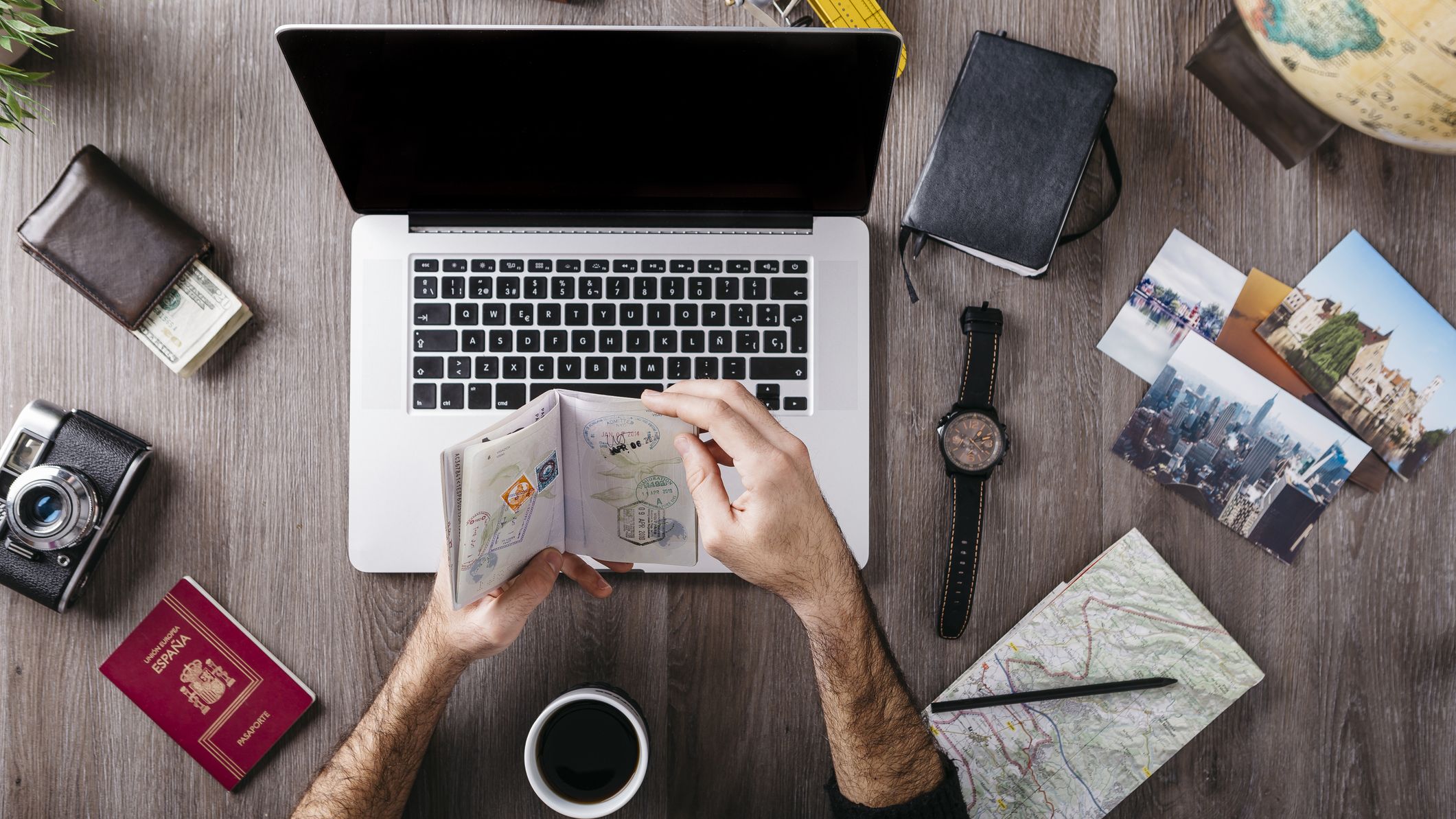 Man looking through his passport drinking coffee in front of an open laptop