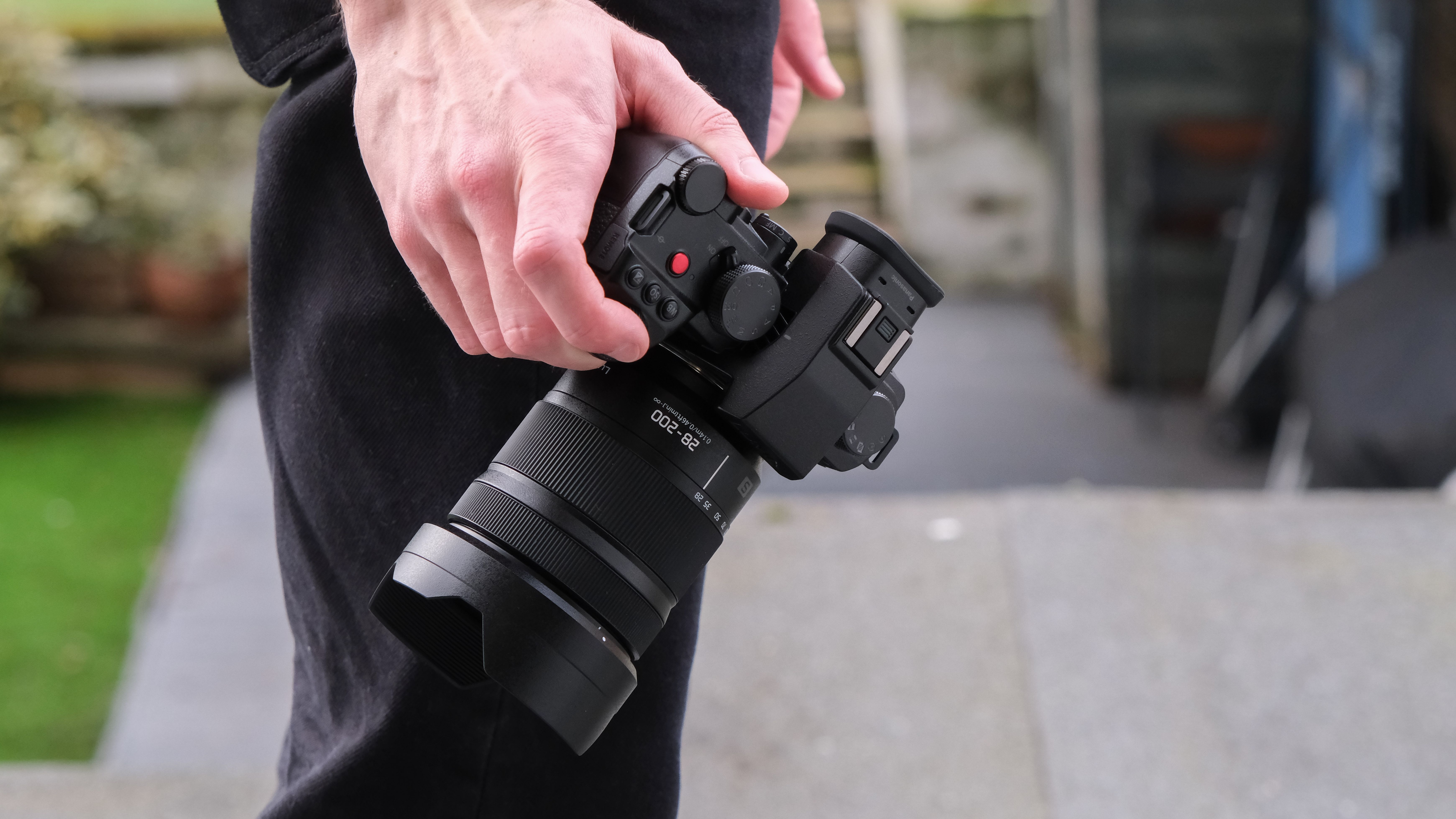 Panasonic Lumix S 28-200mm attached to a camera held in a hand down by a side