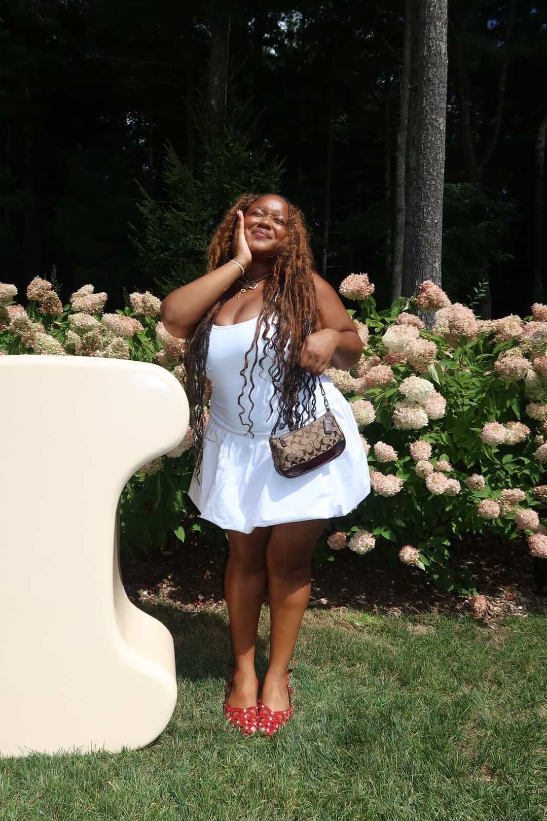 Ashlyn Delaney in a white dress, red shoes, carrying a brown Coach bag