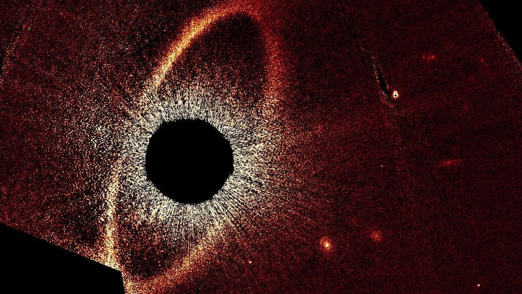 A reddish oval ring of debris surrounds a dark circular region in a Hubble Space Telescope image of the Fomalhaut star system.