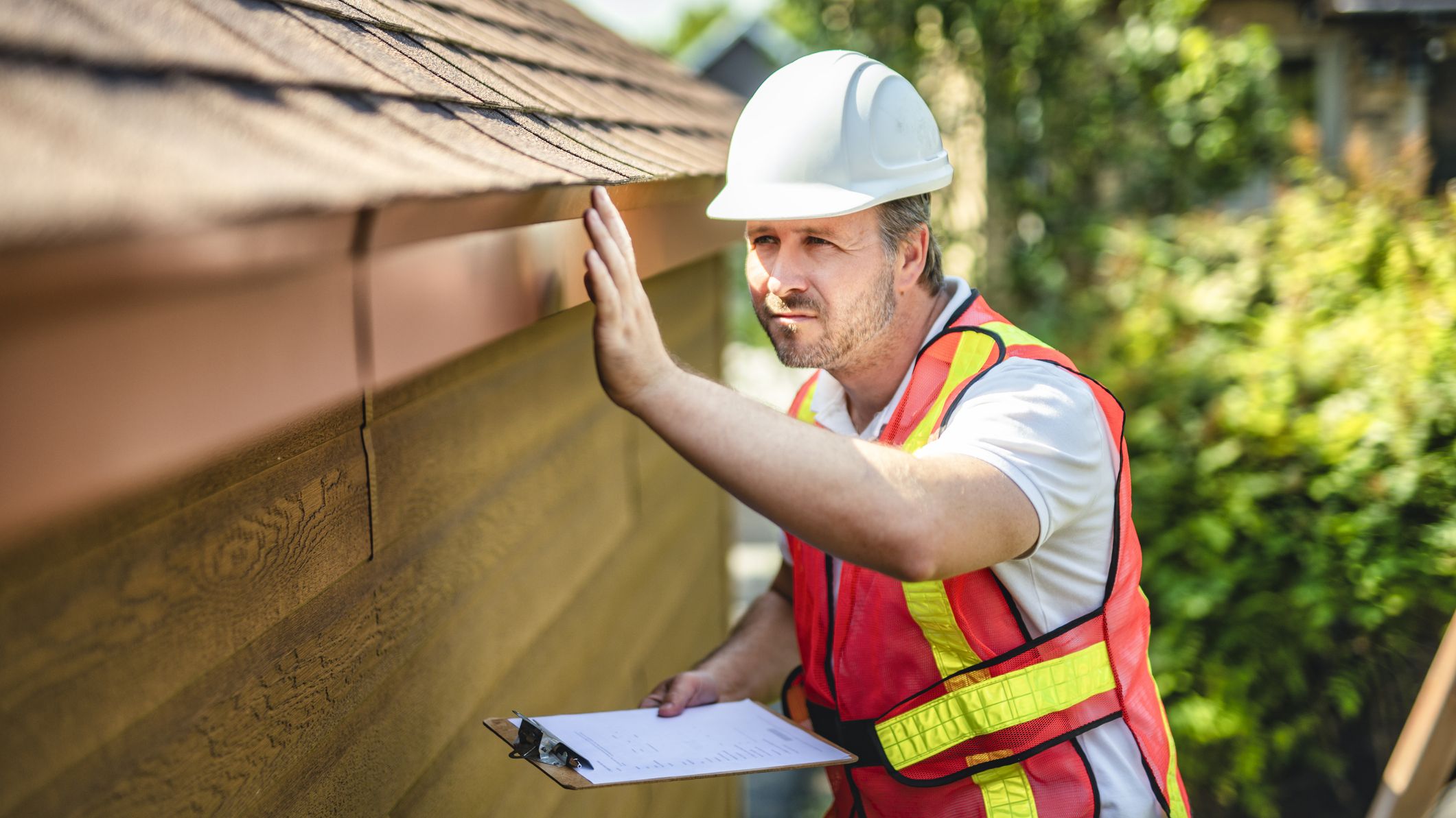 Man inspecting a roof with a clipboard in his hands.