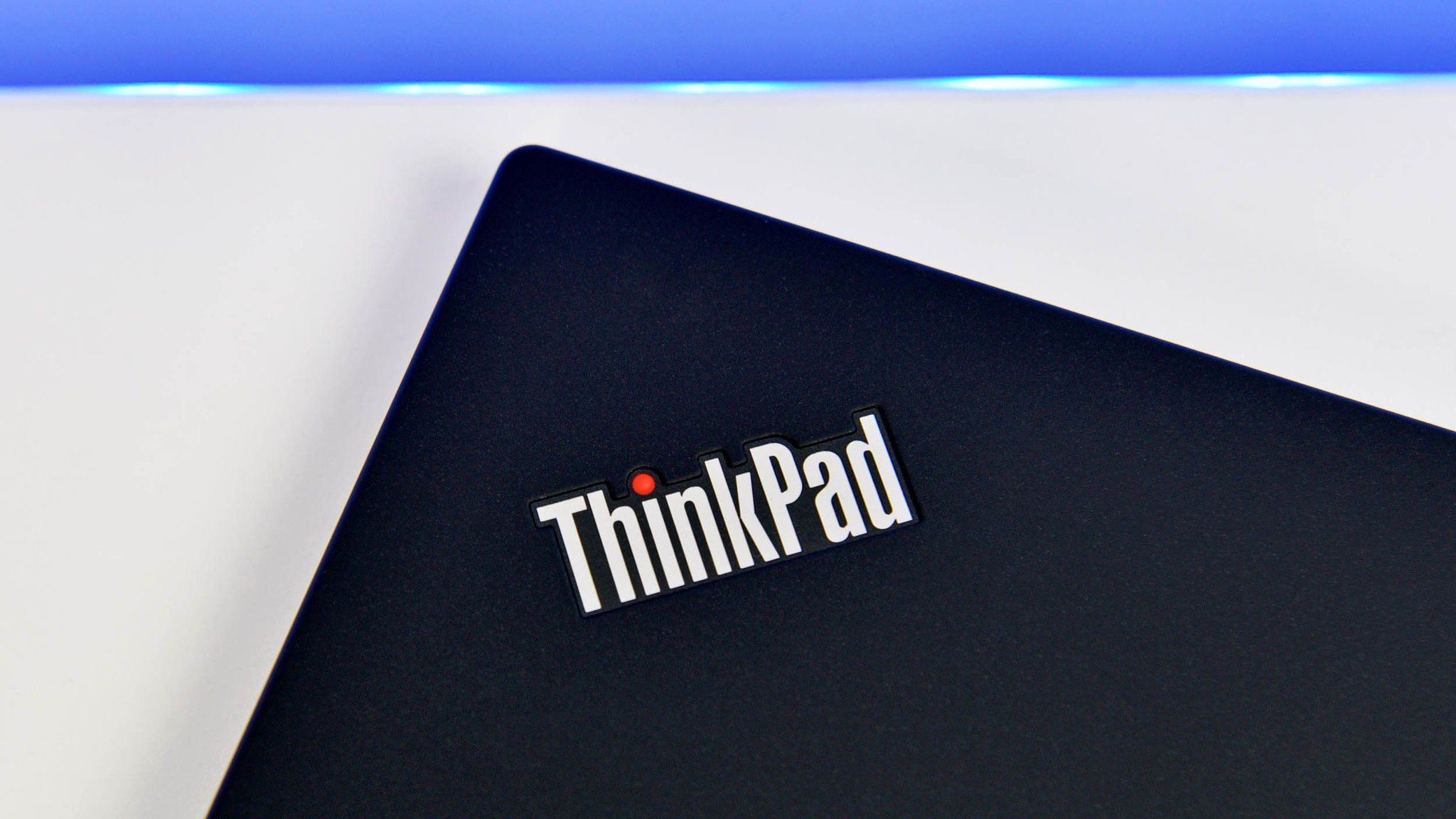 A "ThinkPad" badge on the corner of a black laptop, sitting on a white desk.