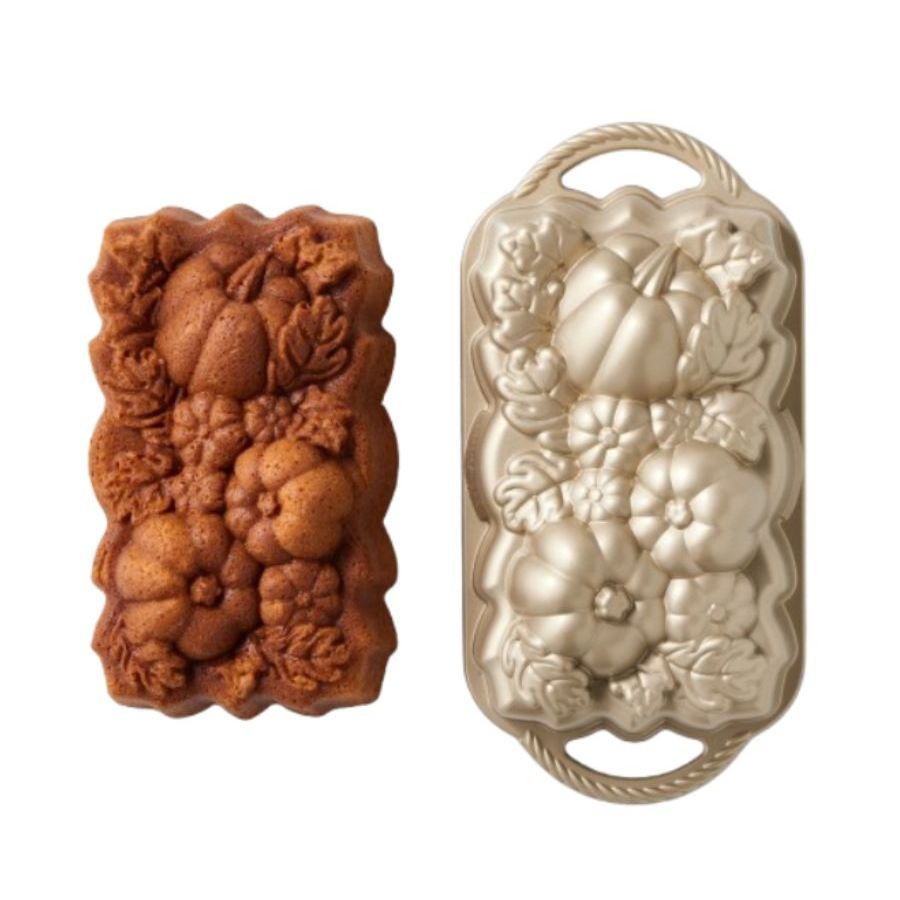 A loaf tin with a pumpkin motif embossed into the top beside a cake with the same design.