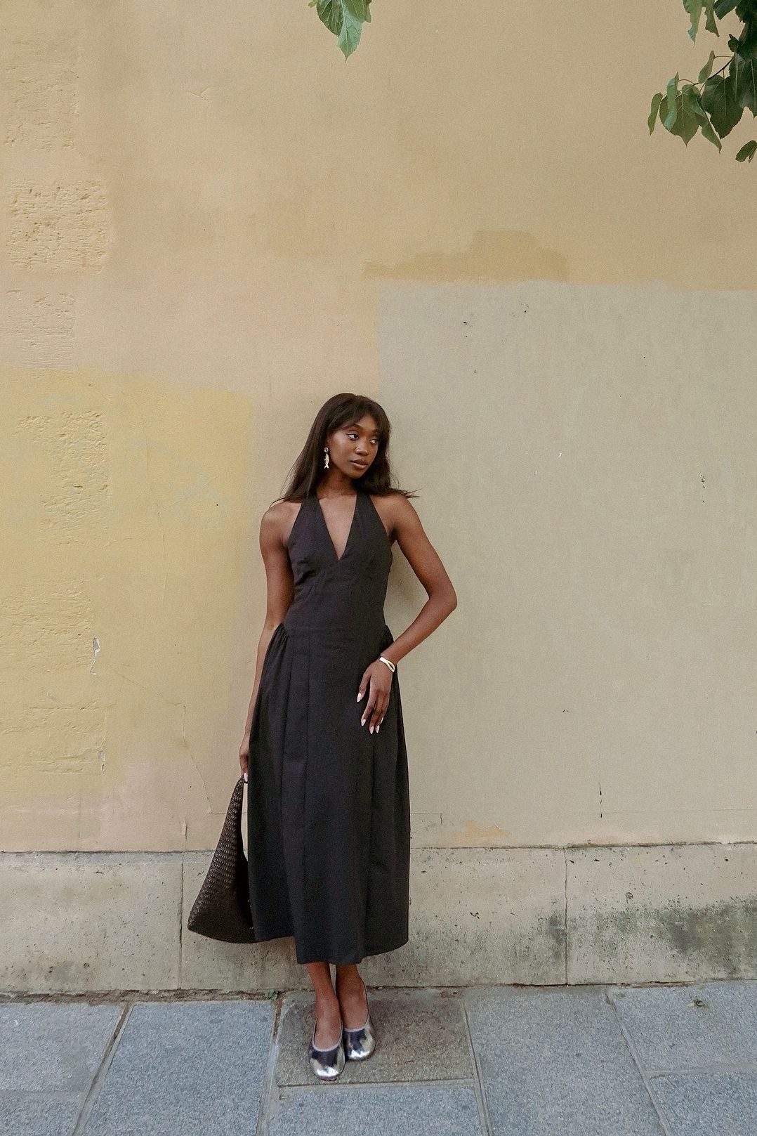 Woman wears black midi dress, silver heels and carries brown woven bag