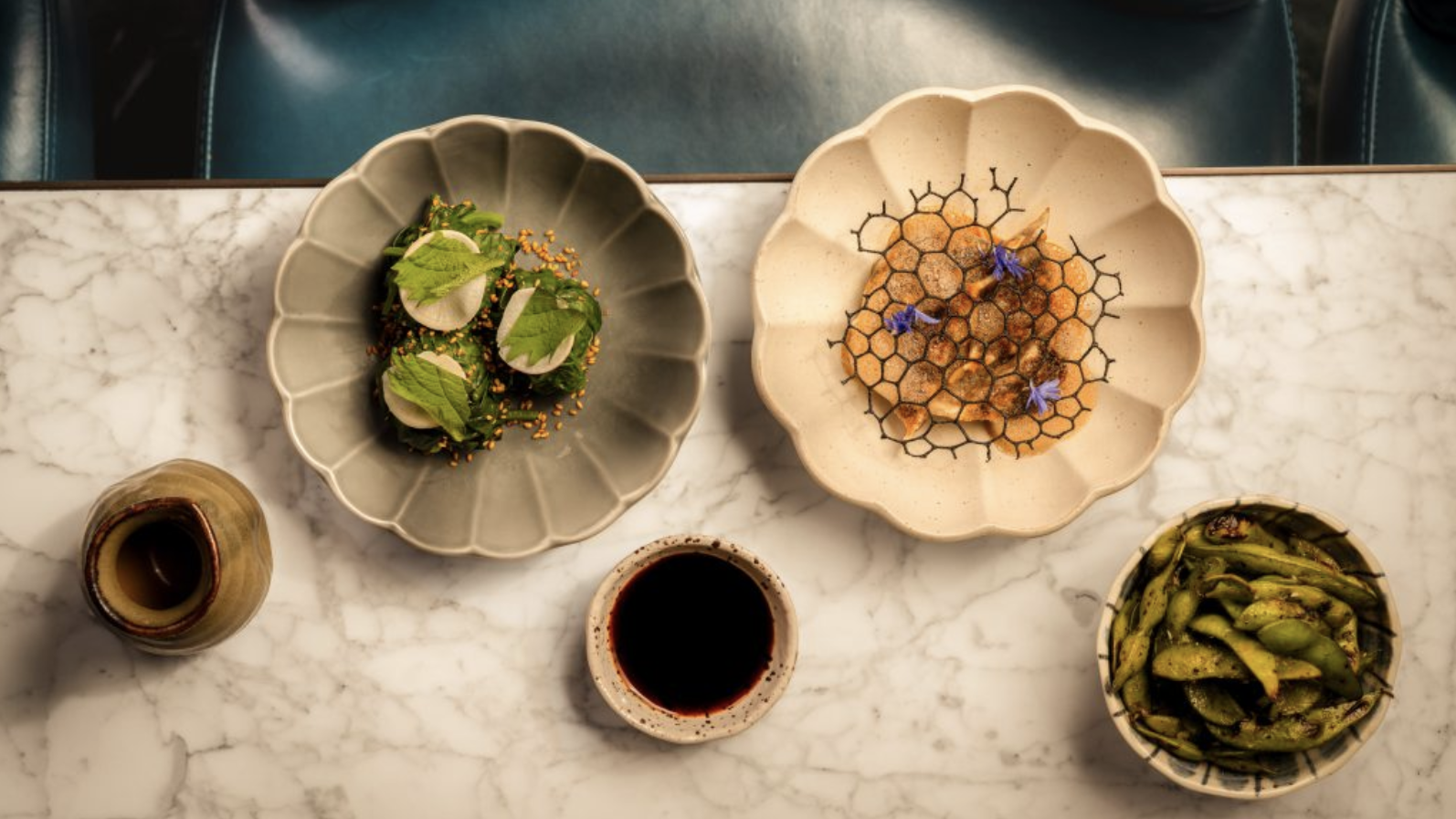 an image of two dishes and a bowl of salted seasame edamame and soy sauce on a table at Aki