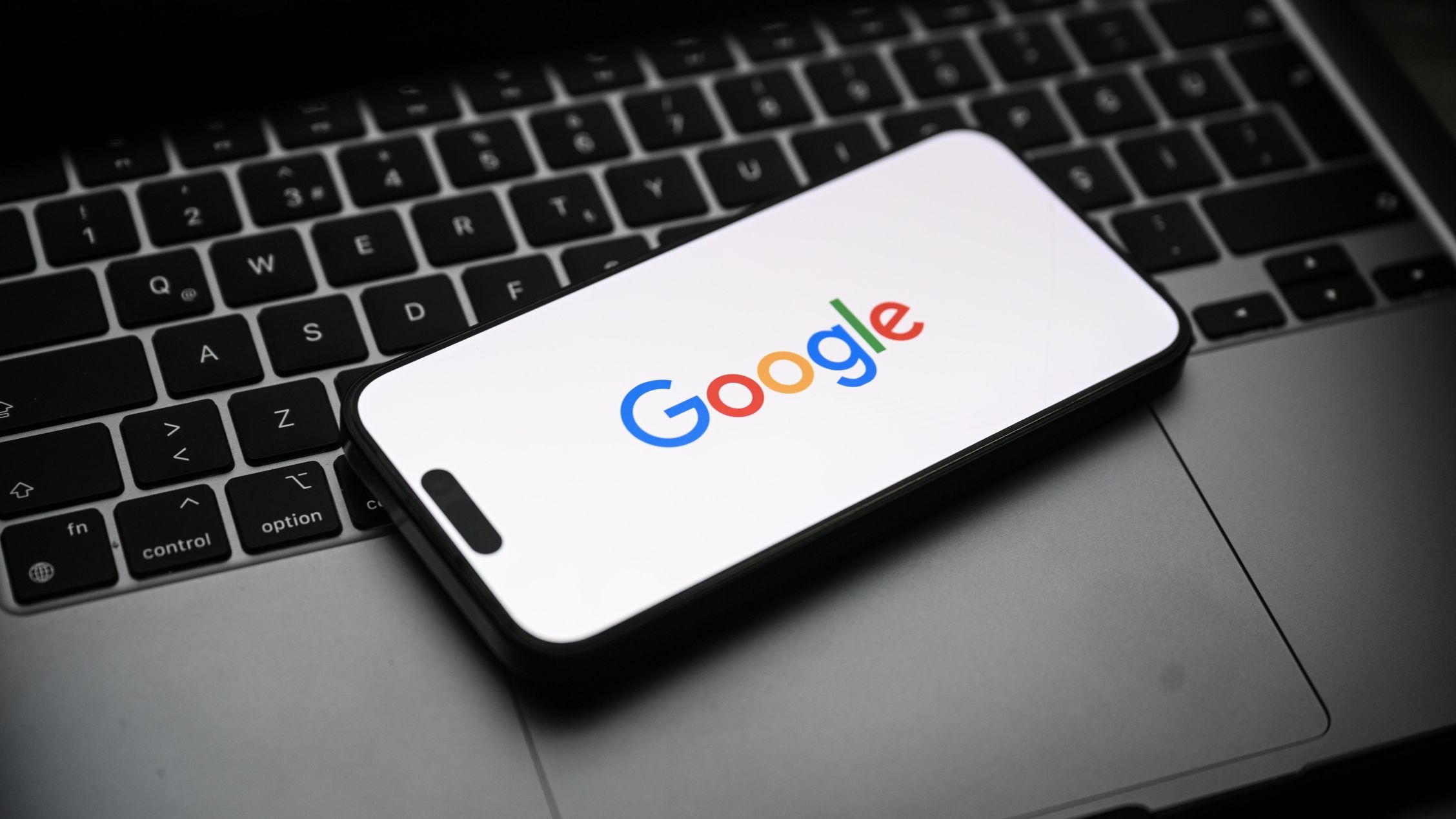 The Google logo displayed on a smartphone that's sitting on top of a laptop.