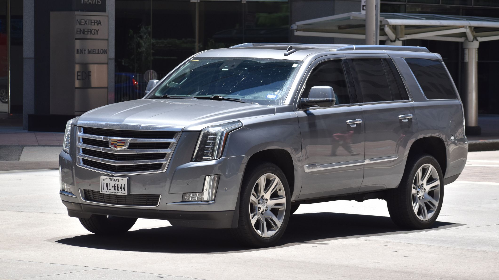 A silver Cadillac Escalade driving down a city street.