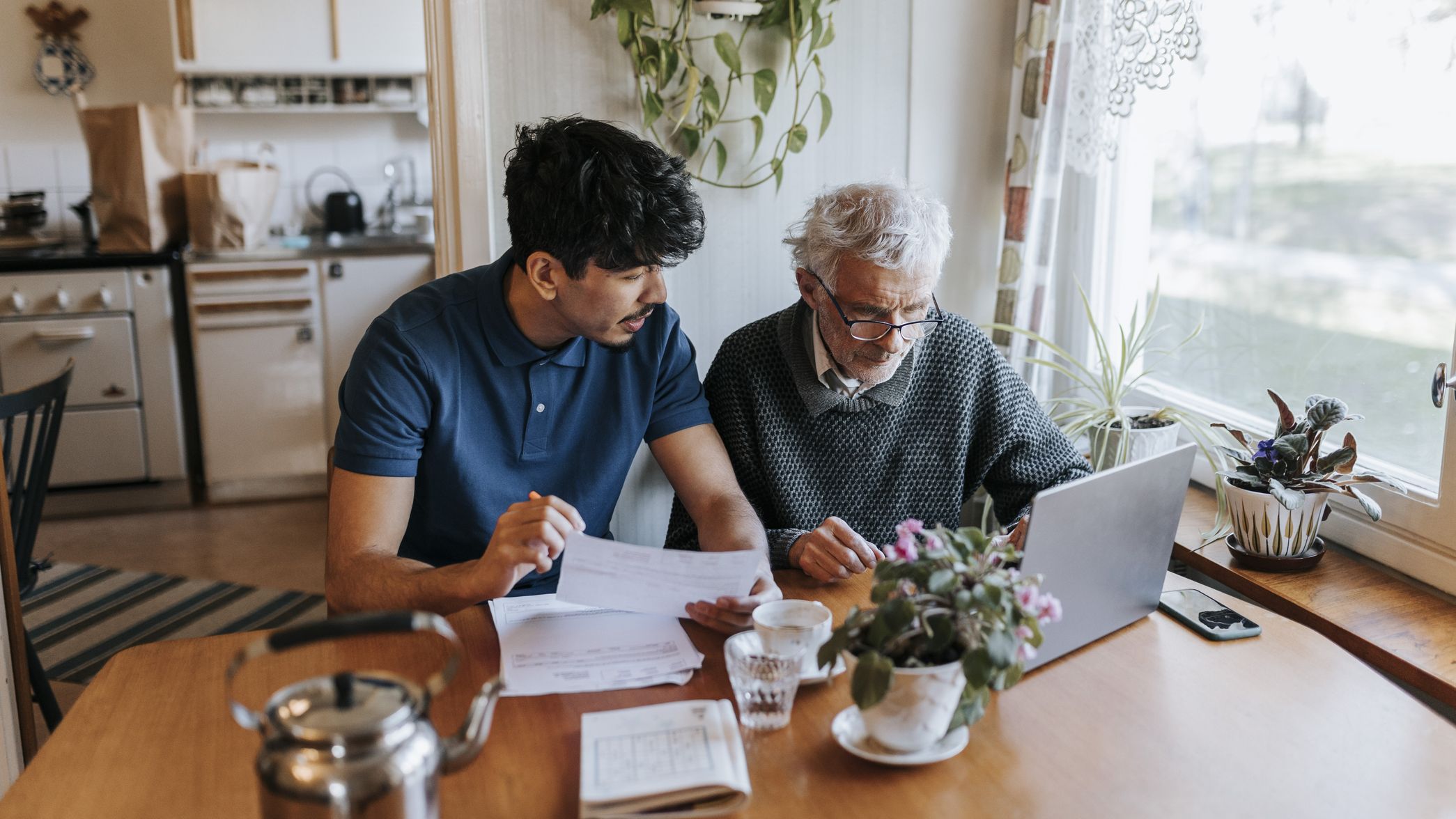 Male caregiver discussing medical reports with senior man using laptop at home