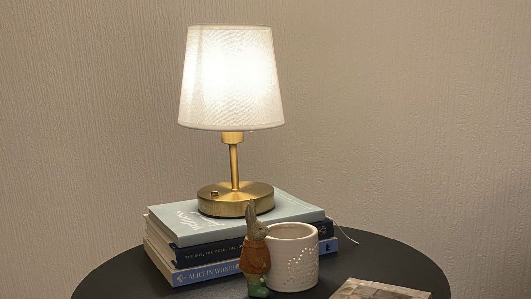 black side table with coasters, stack of books, and cordless lamp