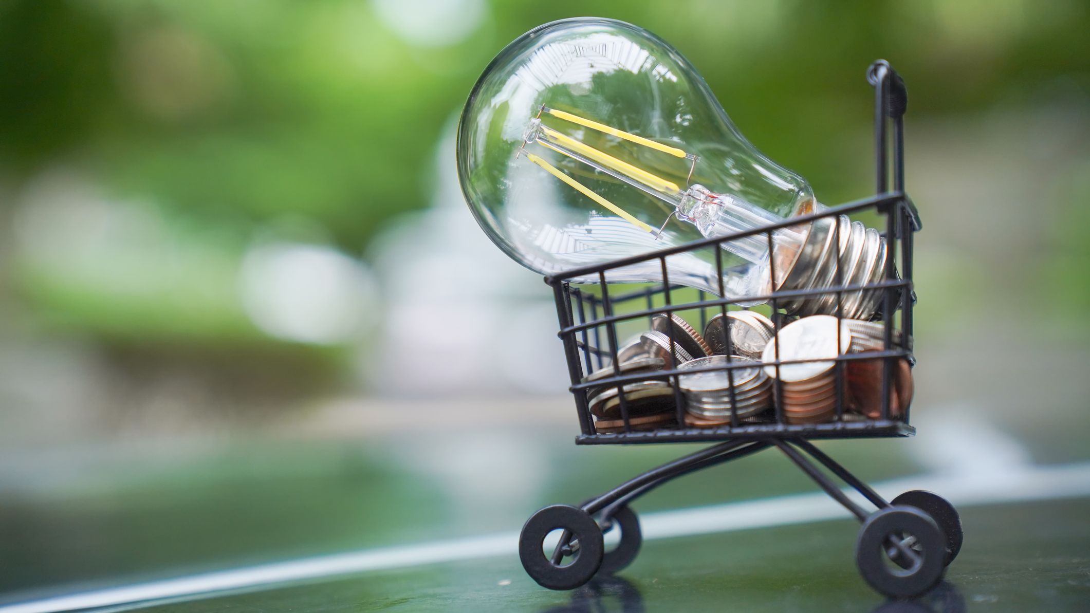 a light bulb sitting on top a stack of coins in a shopping cart indicating energy savings