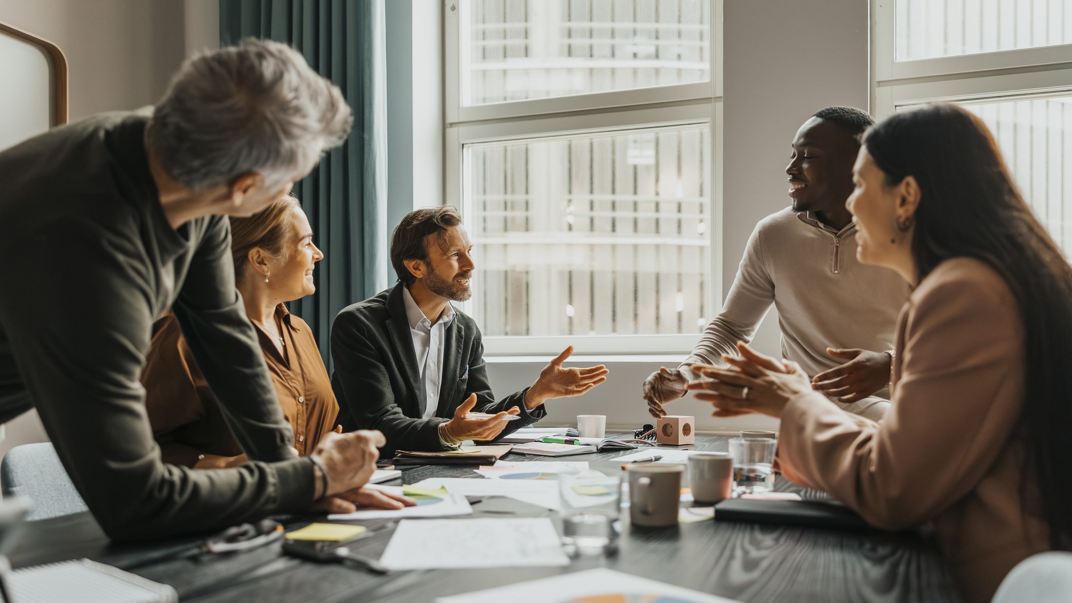 A team of smiling business professionals discuss ideas while sitting around a table in a meeting room