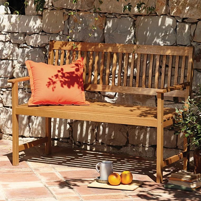 wooden garden bench next to stone wall with pillow on it