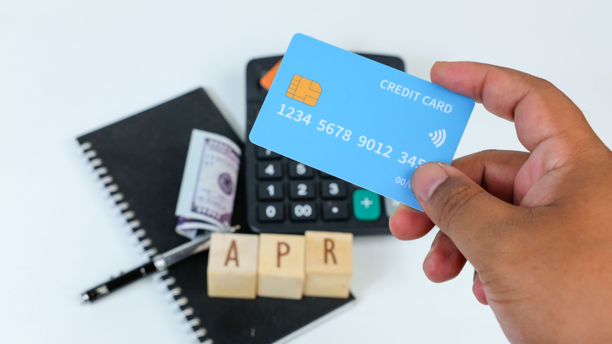 a hand holding a credit card with Scrabble blocks reading APR next to a calculator below the hand