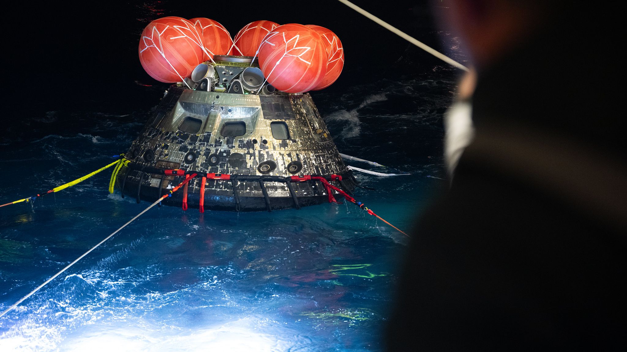 The Orion spacecraft is pulled from the sea after splashdown at night.