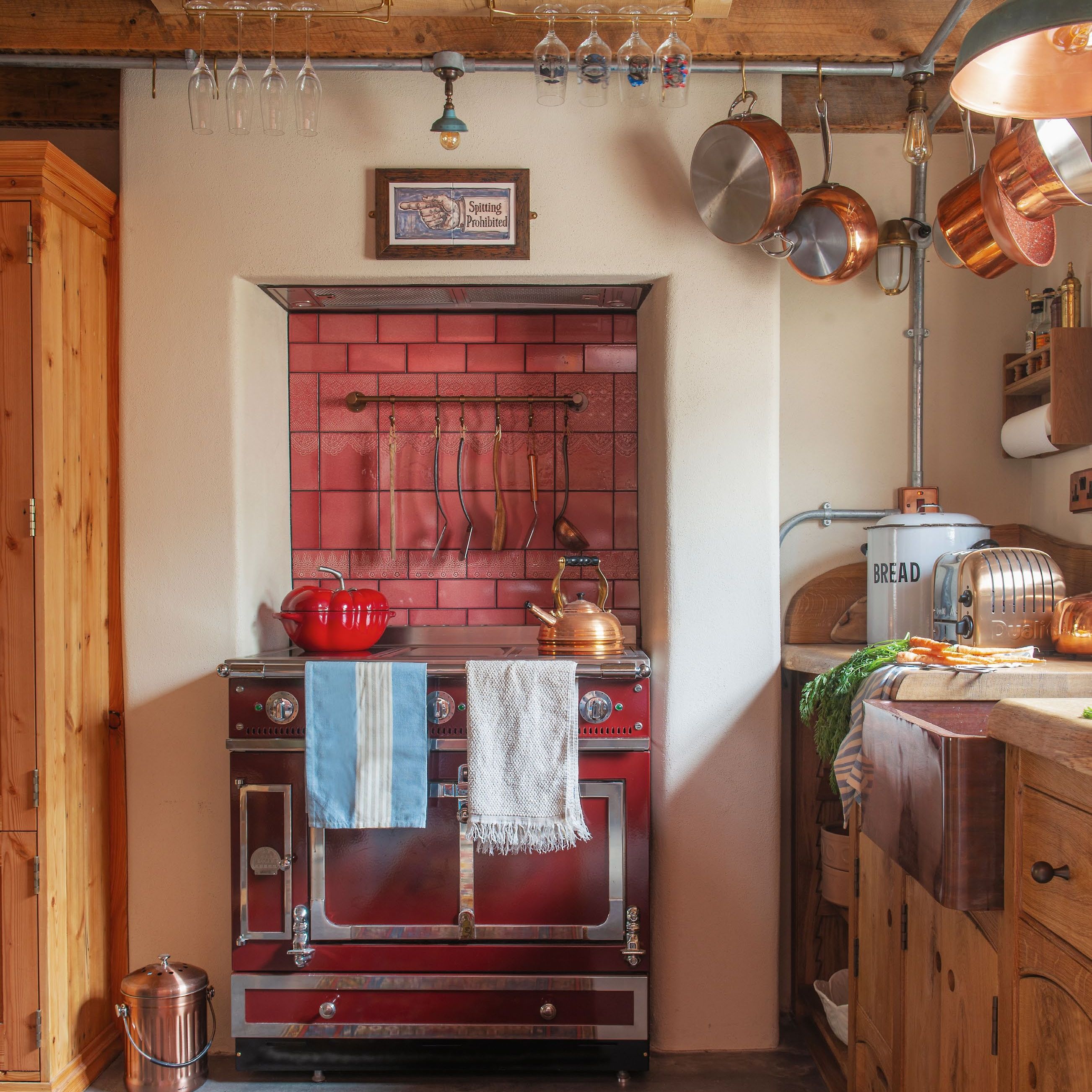 range cooker in the recess of a former fireplace, with splashback of bright terracotta coloured tiles and copper pans hanging above