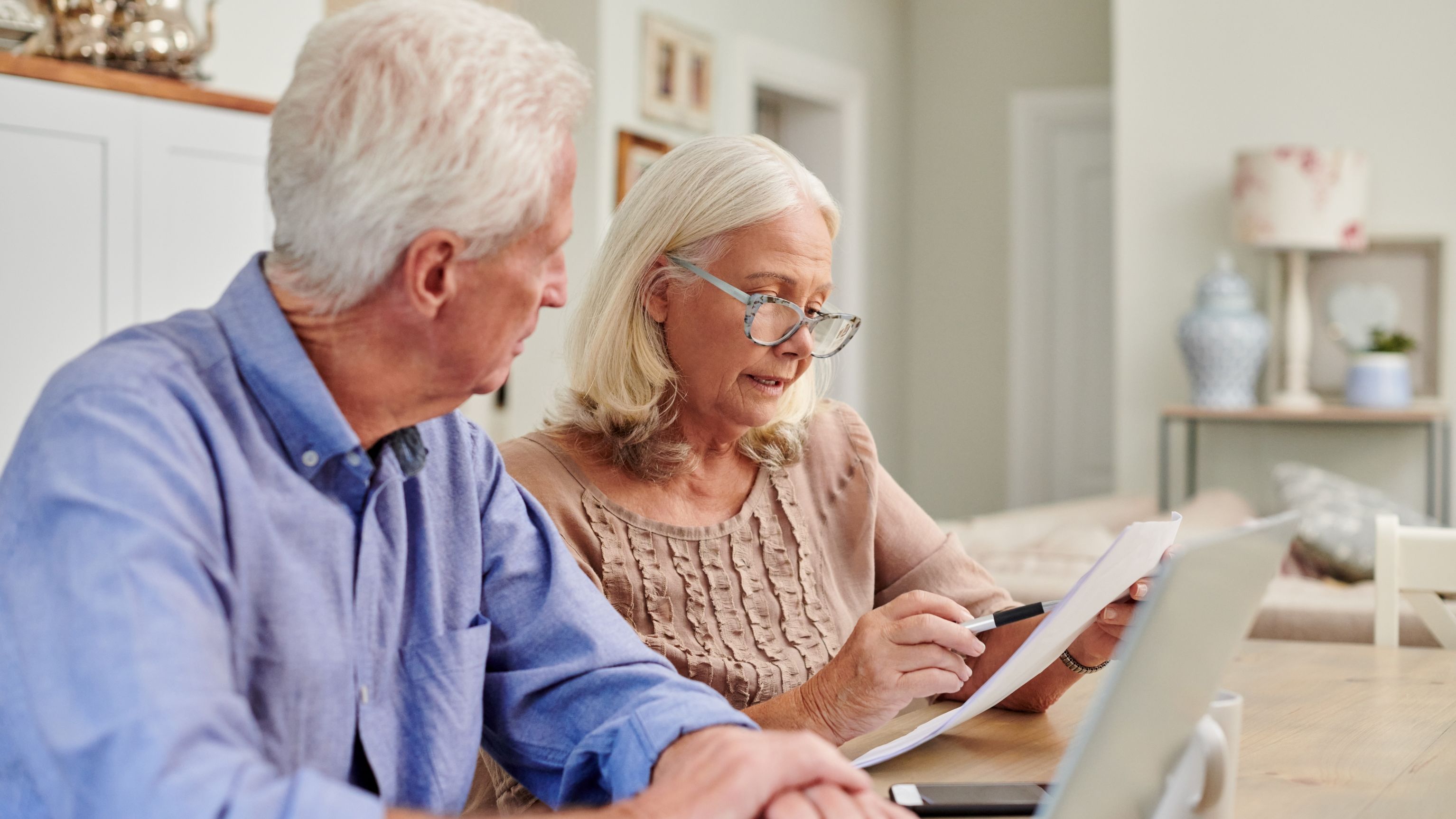 A senior couple reviews paperwork while sitting at their dining room table.