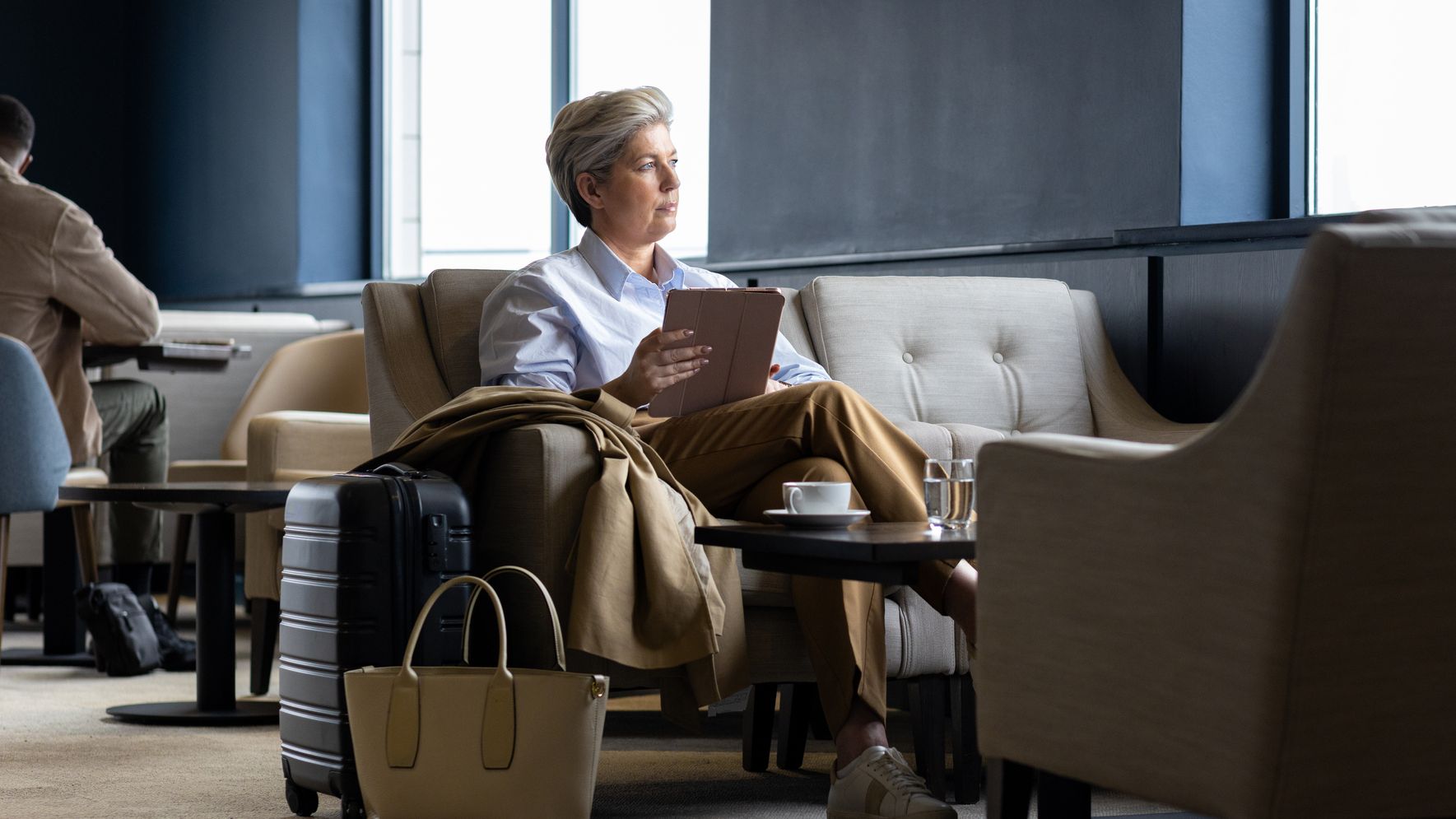 Woman with an ipad looking out the window of an airport lounge.