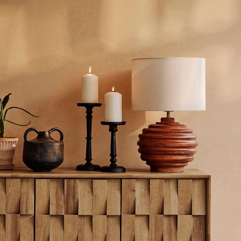 Beige wall with wooden sideboard, black candlestick holders and a wooden table lamp.