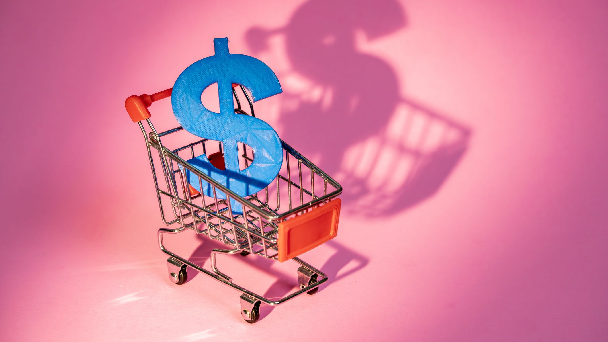 Shopping cart carrying a big blue dollar sign on pink background