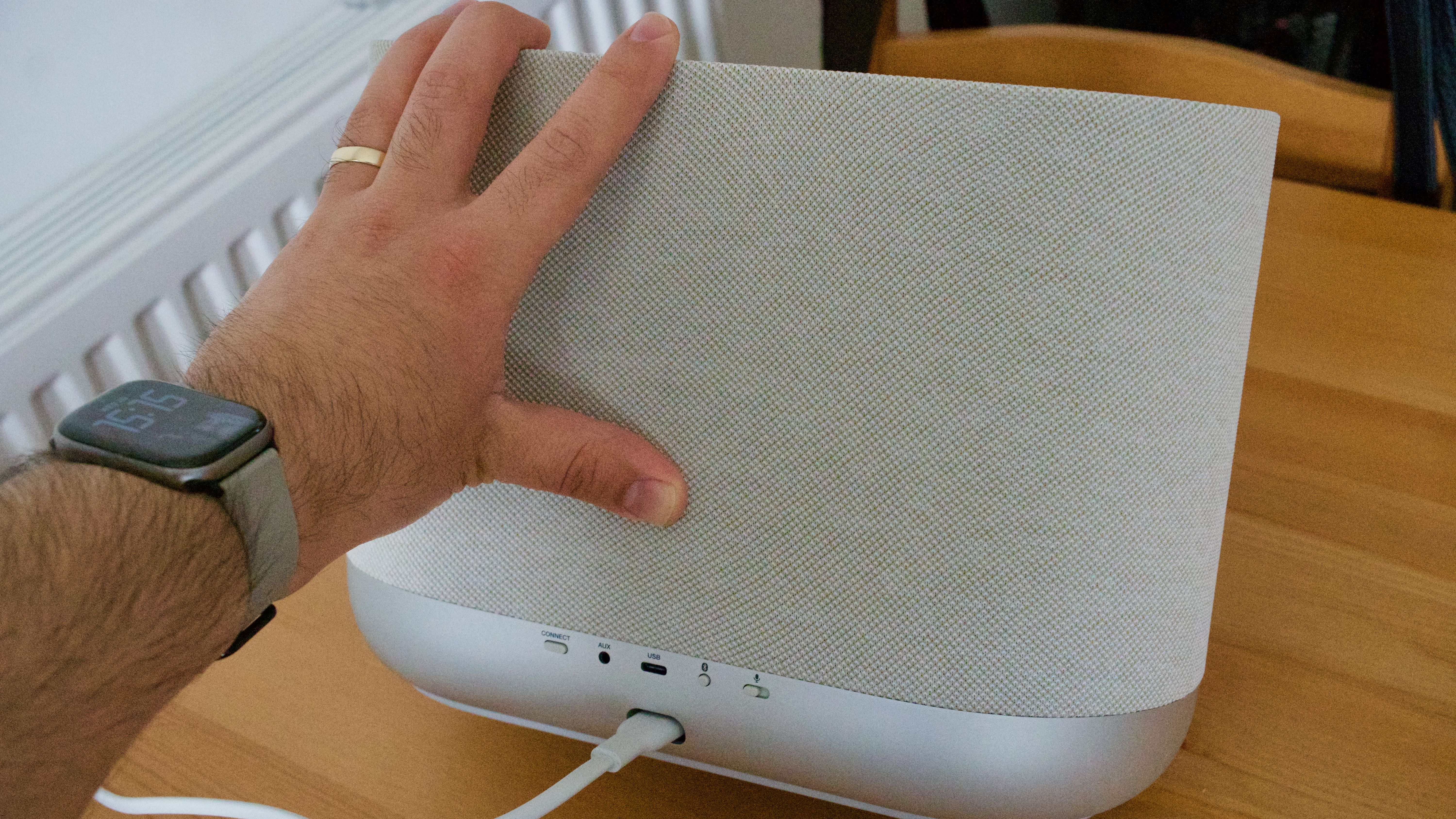 A man's hand rolls the Denon Home 400 home speaker partially onto its side, revealing the rear panel.