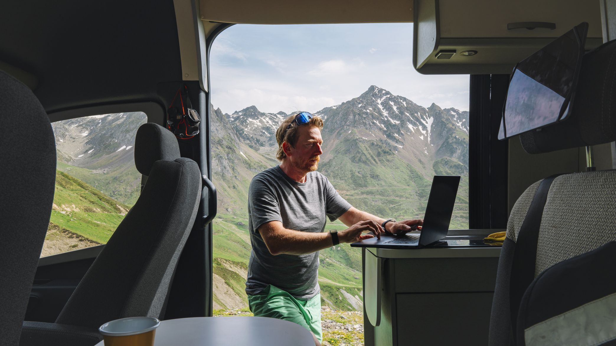 A man catches up on a few emails on his laptop from his campervan as the sun sets.