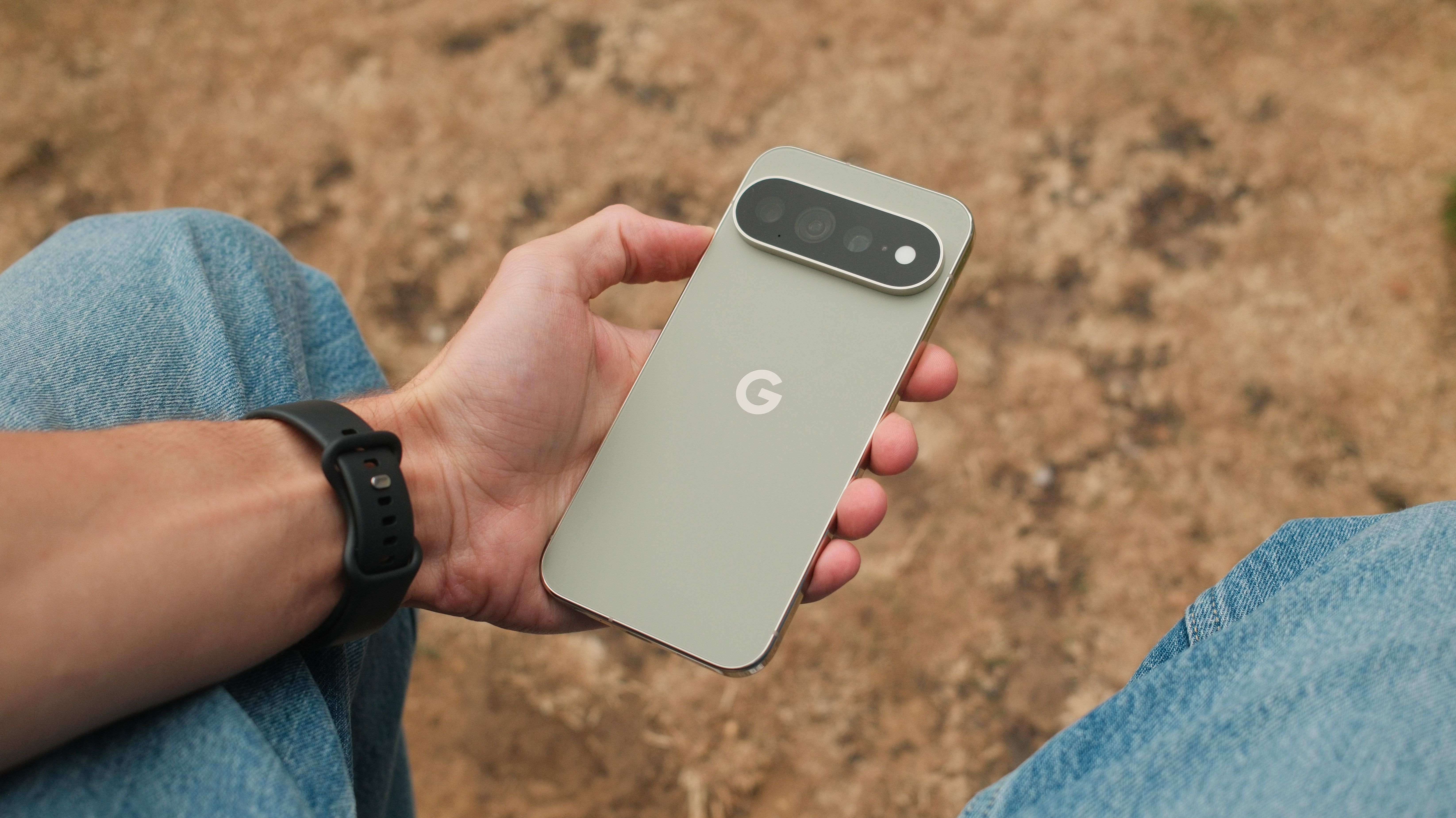 Google Pixel 11 Pro XL held in one hand outdoors, showing its pale green rear panel and horizontal camera bar.
