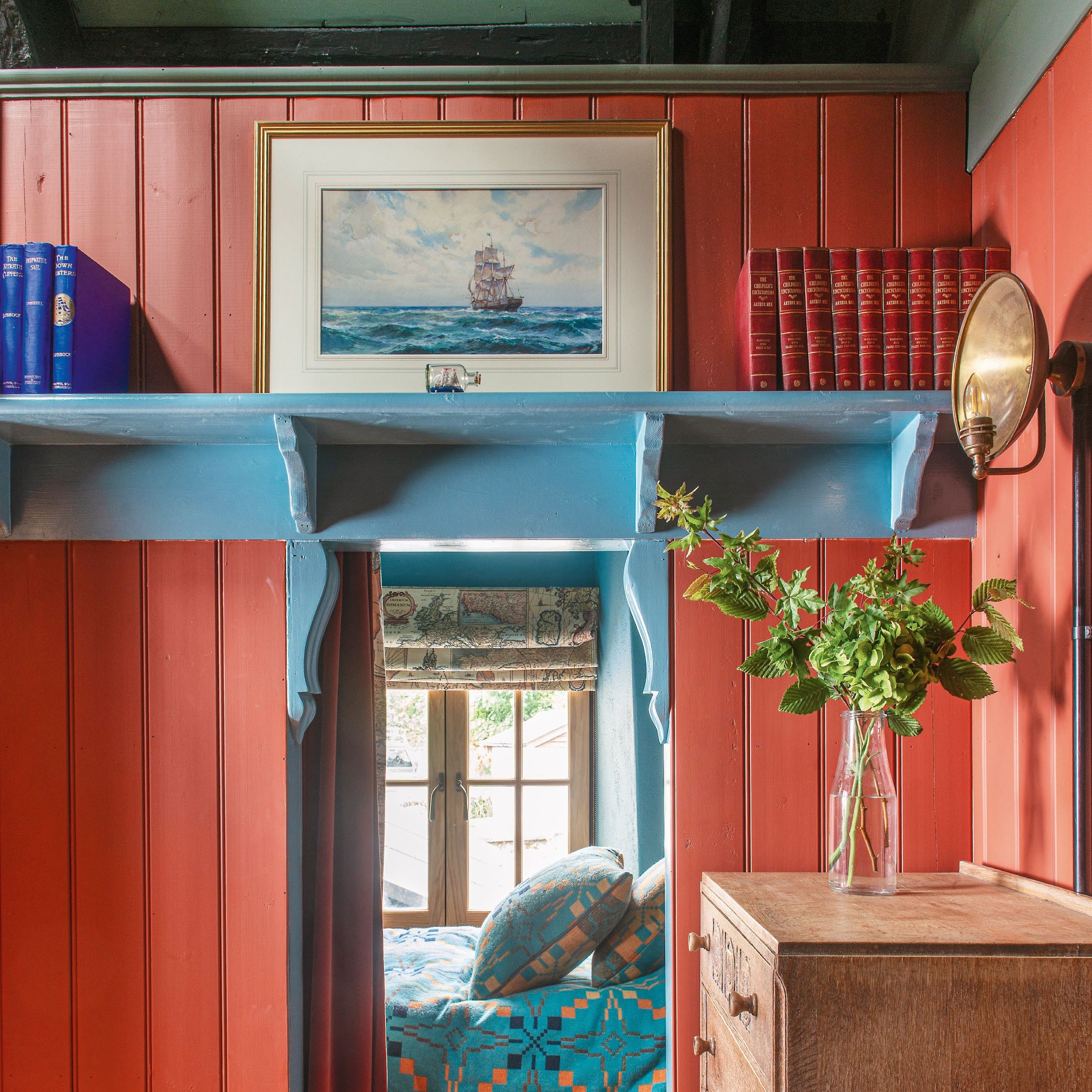 View through a small doorway into a bedroom, with red painted wood panelling and bright blue shelf above doorway