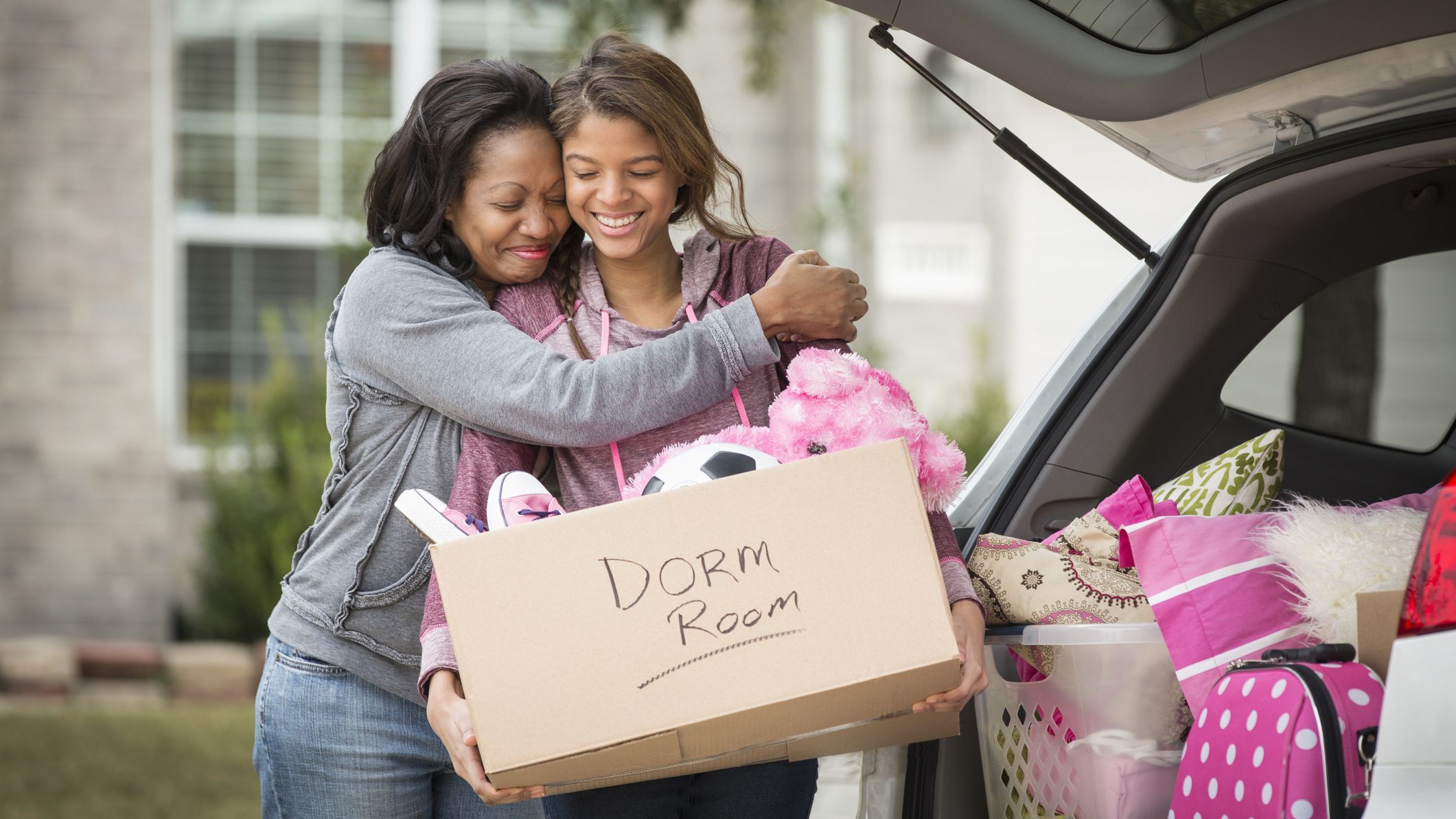 A mother and daughter hug while packing up the car to go to college.